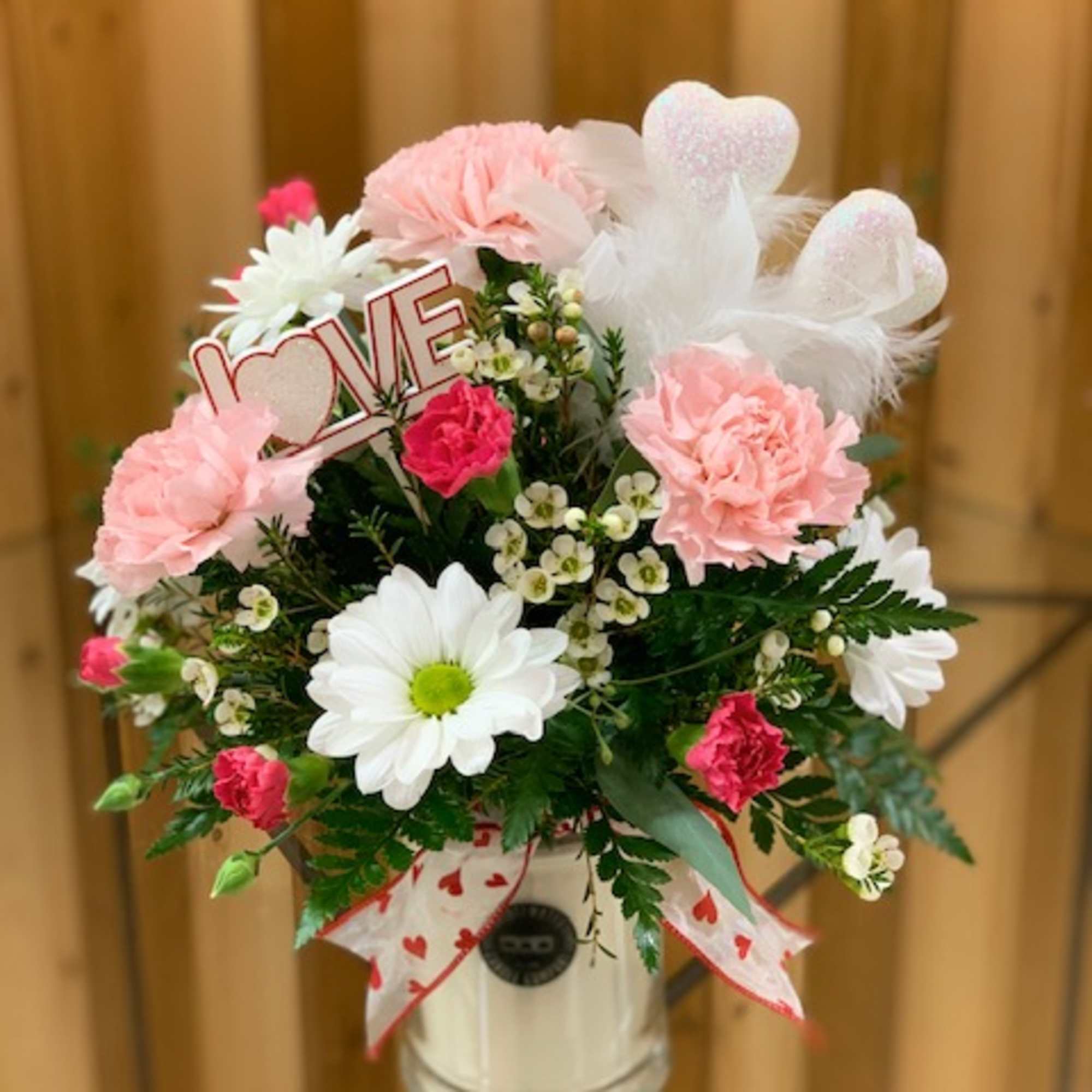 Pink and white floral arrangement in a glass vase with a LOVE sign