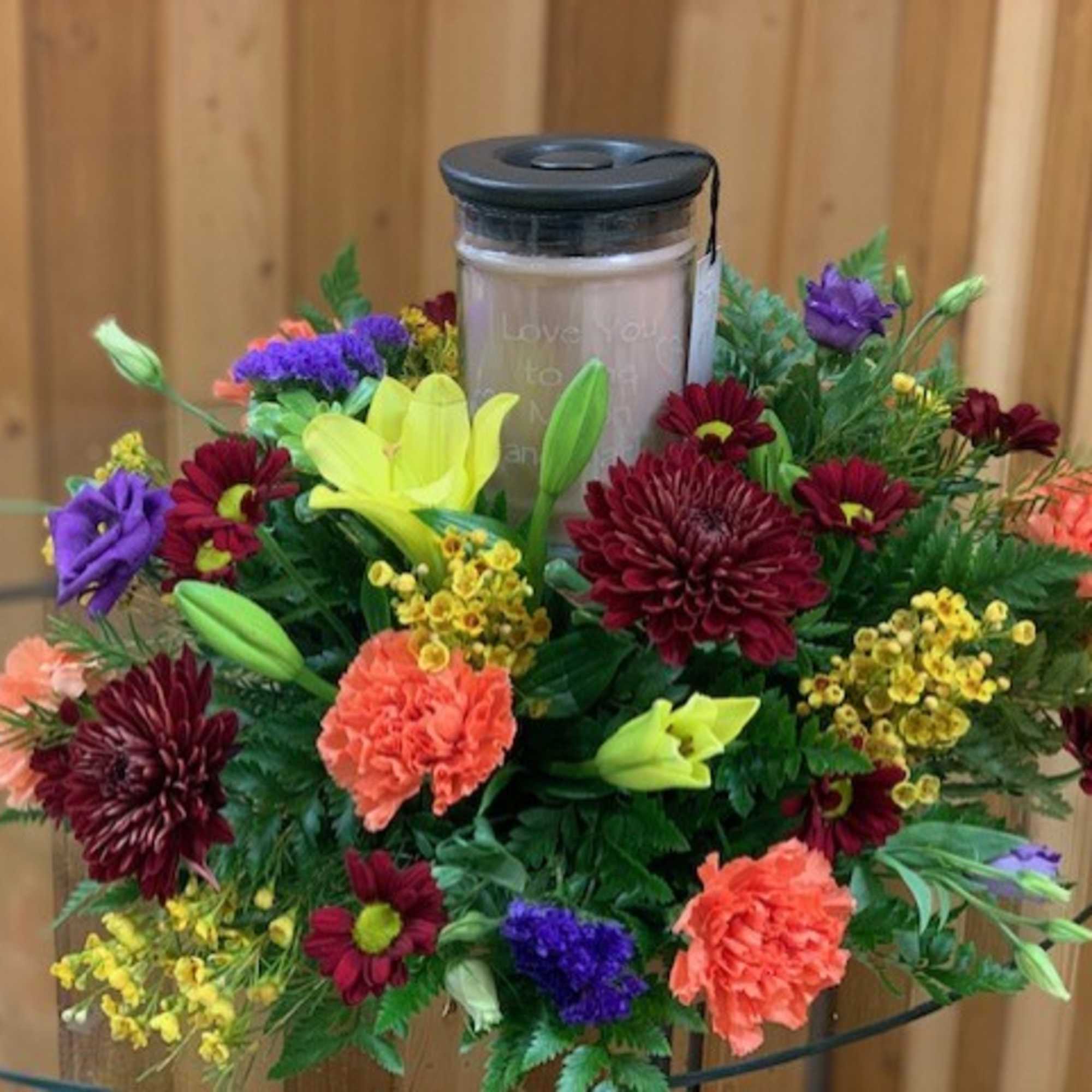Floral arrangement around a memorial candle in a glass jar