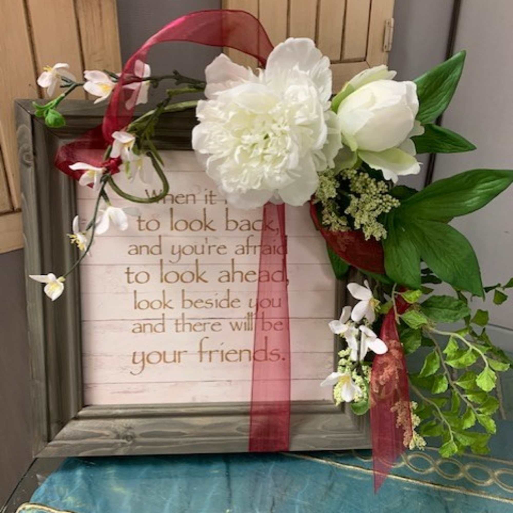 White flowers and greenery on a framed sign with a red ribbon