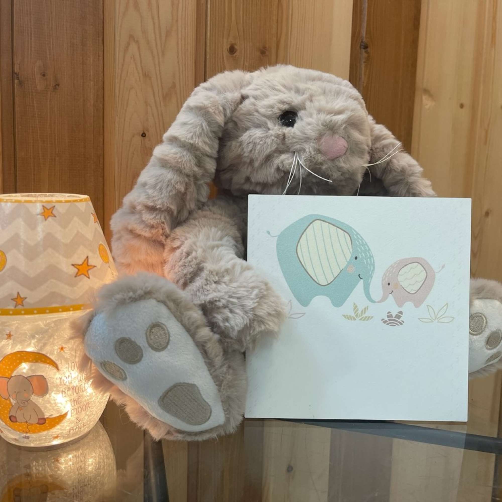 Plush bunny holding a baby card beside a lit elephant lamp