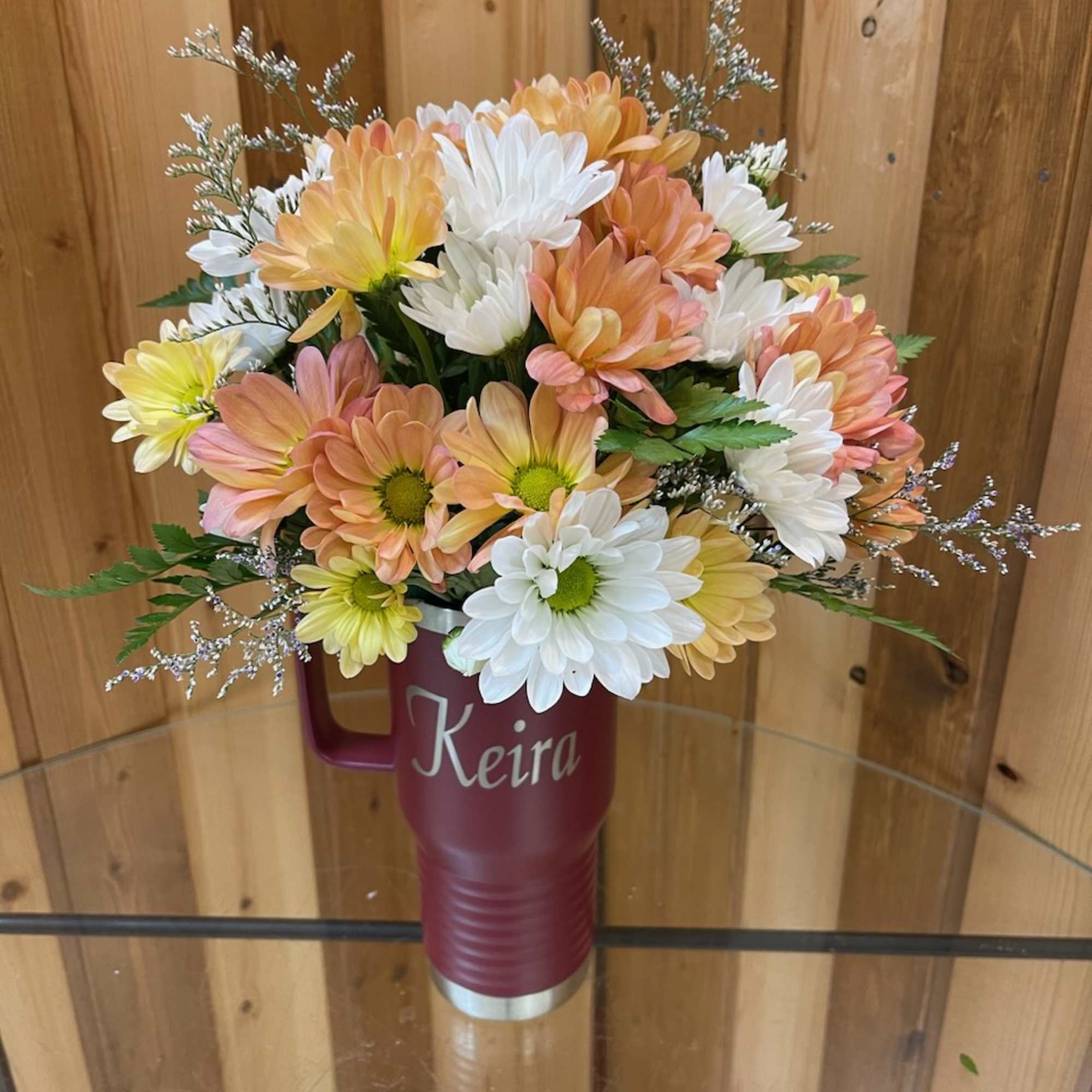 Bouquet of peach, white, and yellow daisies in a maroon tumbler vase