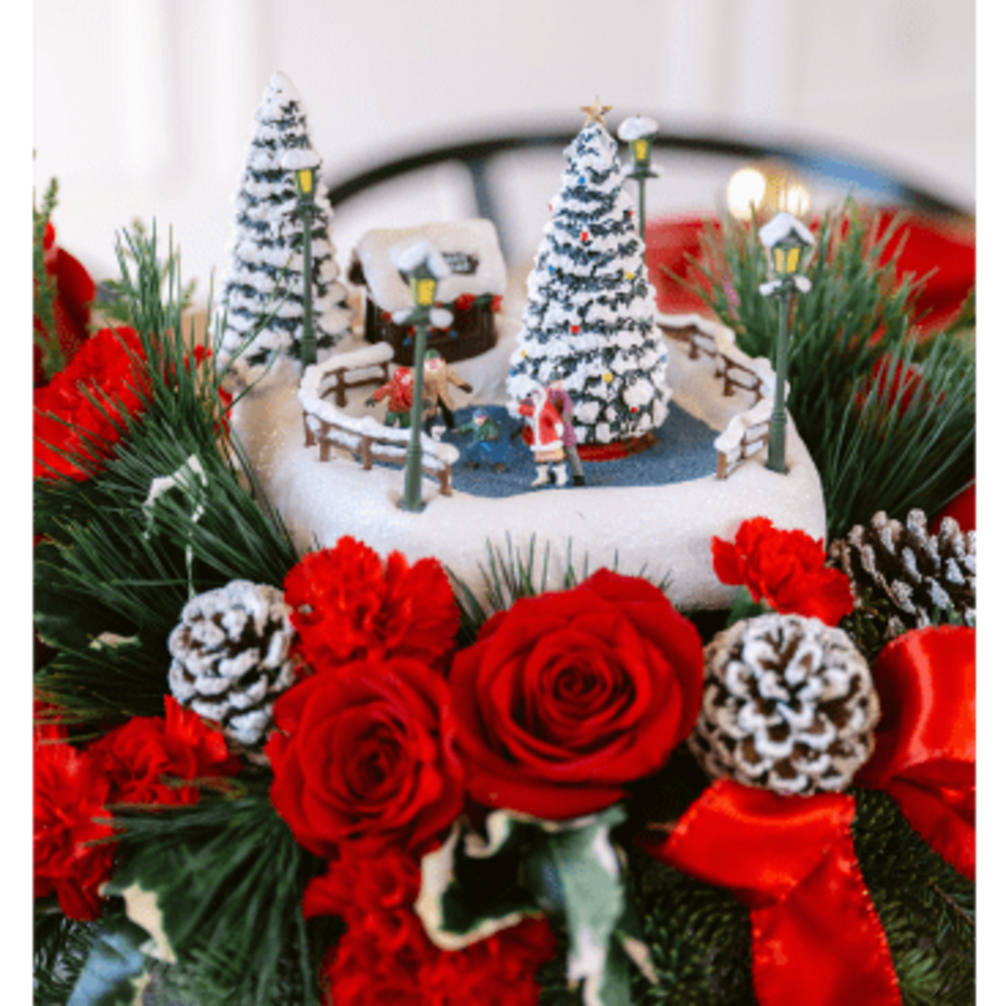 Christmas floral arrangement with red roses, pinecones, and a miniature winter village