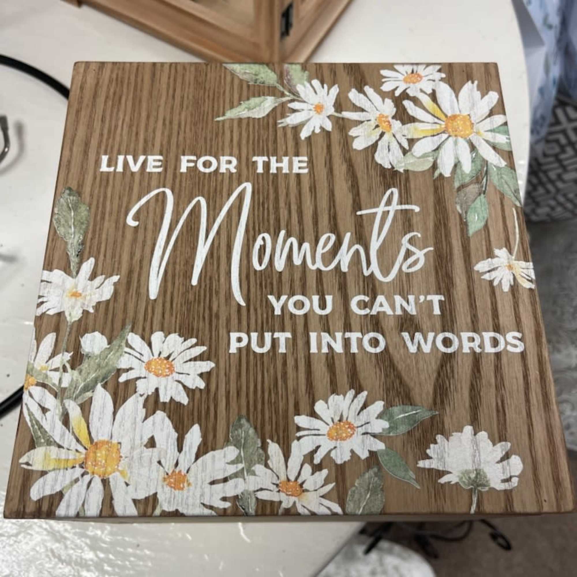 Wooden sign with daisies and the words "Live for the moments you can't put into words"