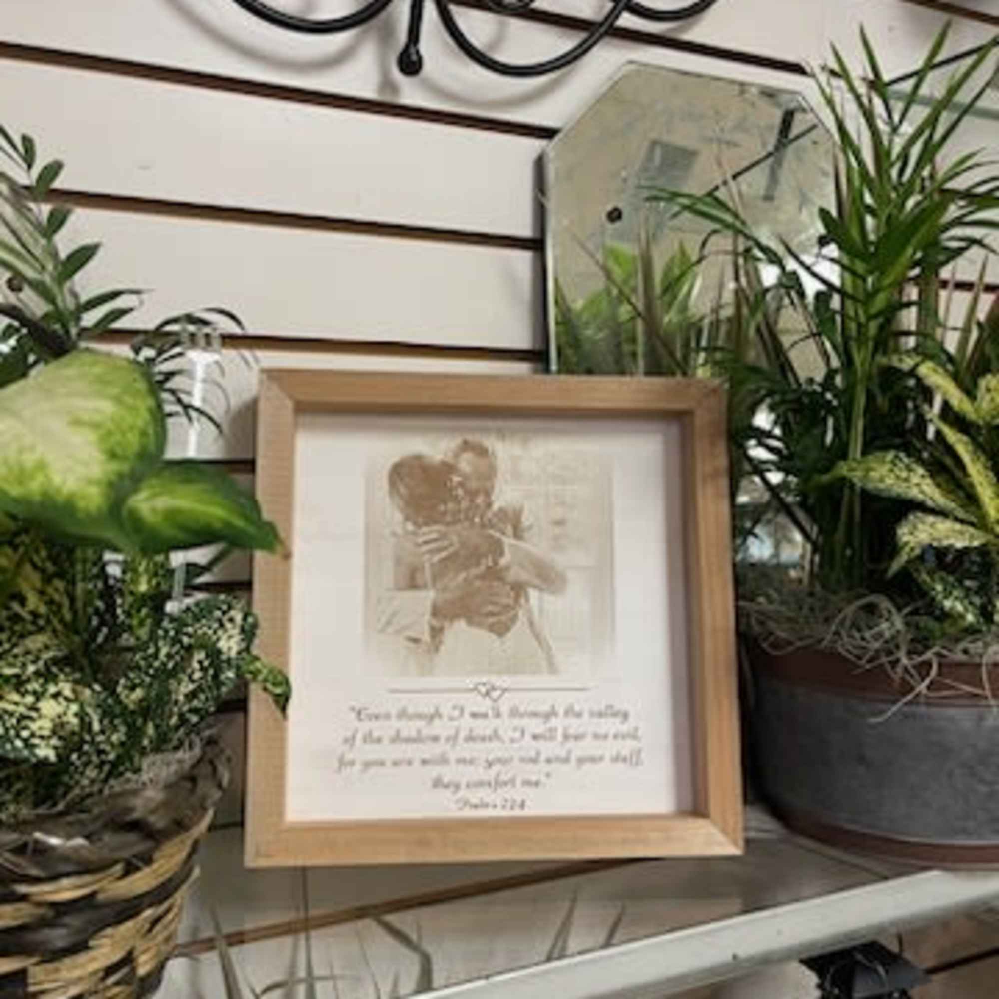 Framed memorial print surrounded by potted plants