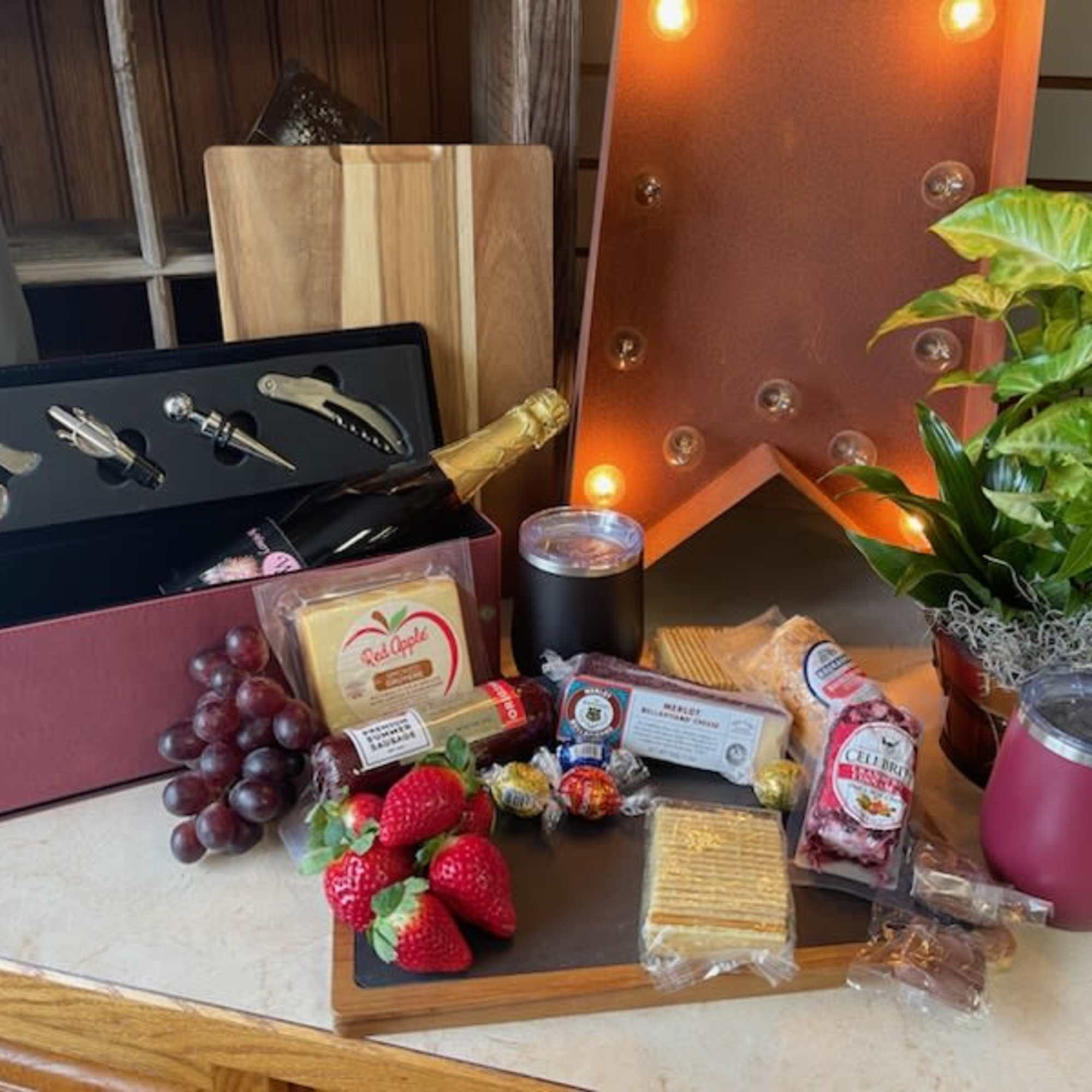 Gift basket with champagne, snacks, fruit, and a potted plant