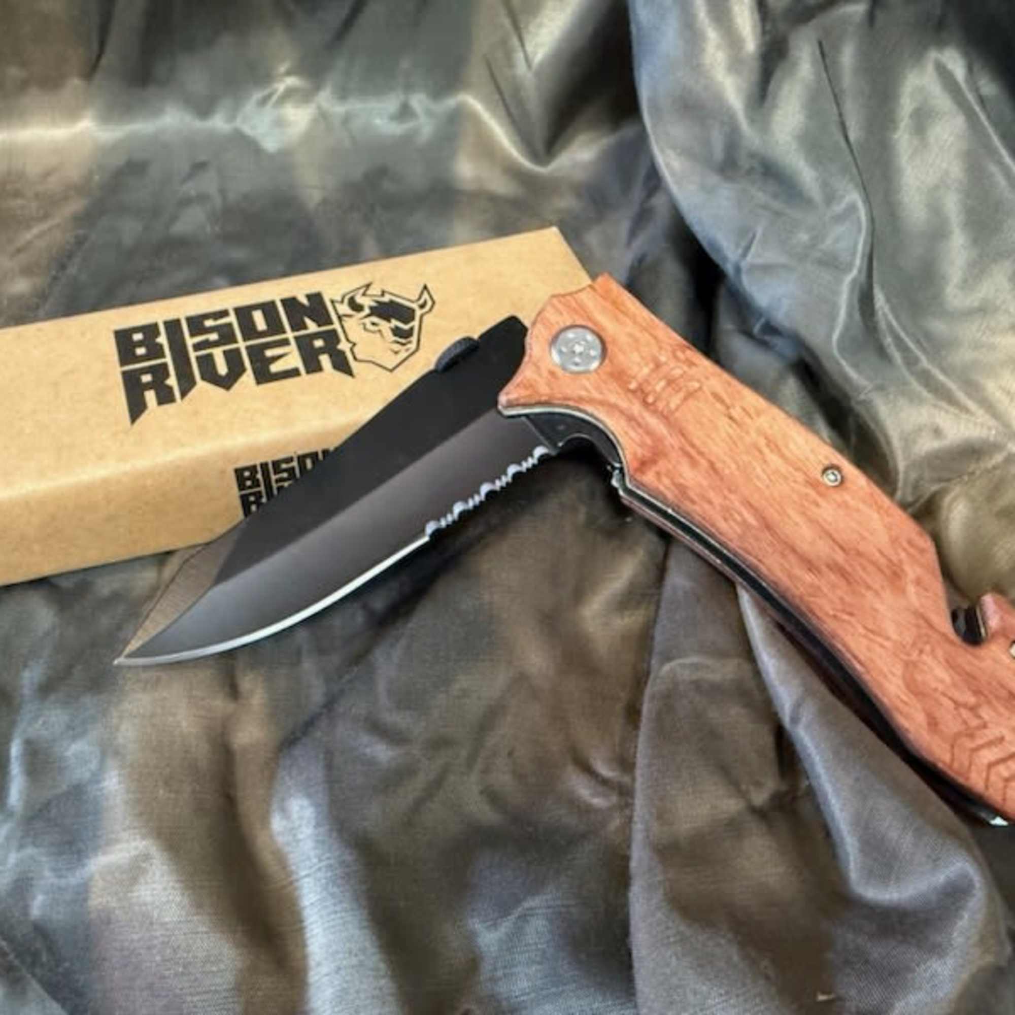 Folding knife with a wood handle beside a branded box