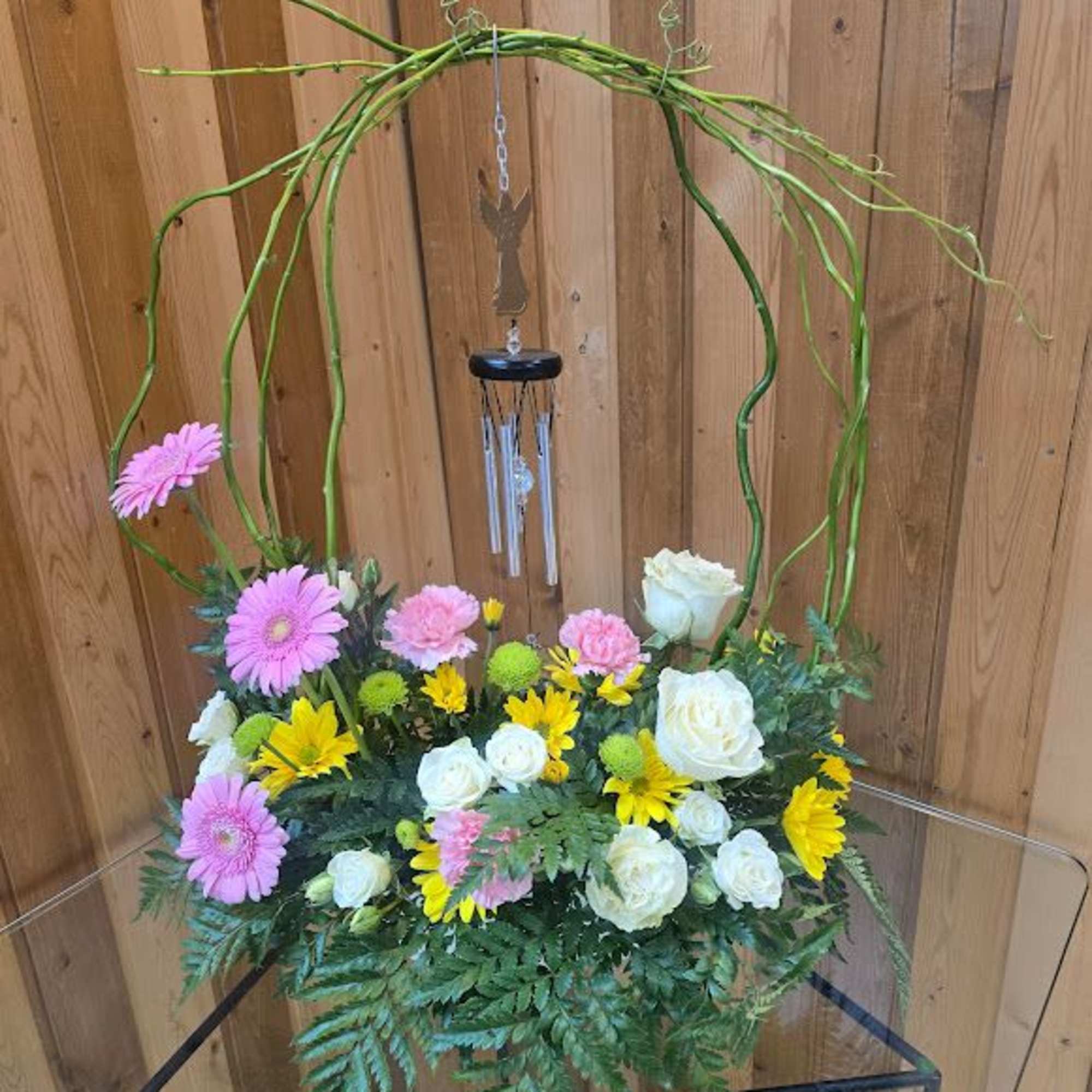 Mixed flower arrangement with pink, white, and yellow blooms under a hanging wind chime