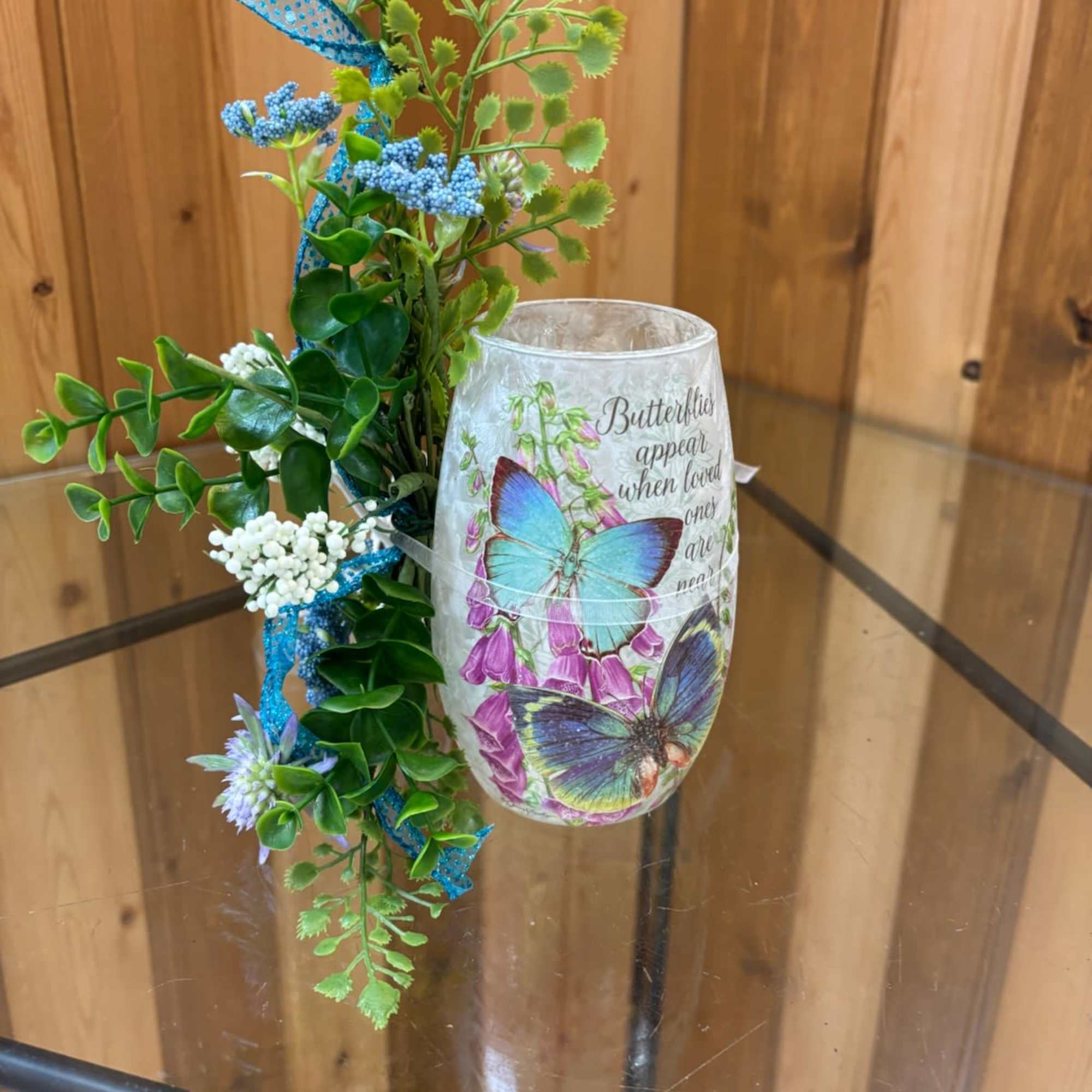 Butterfly-themed glass candle holder with faux greenery and blue accents