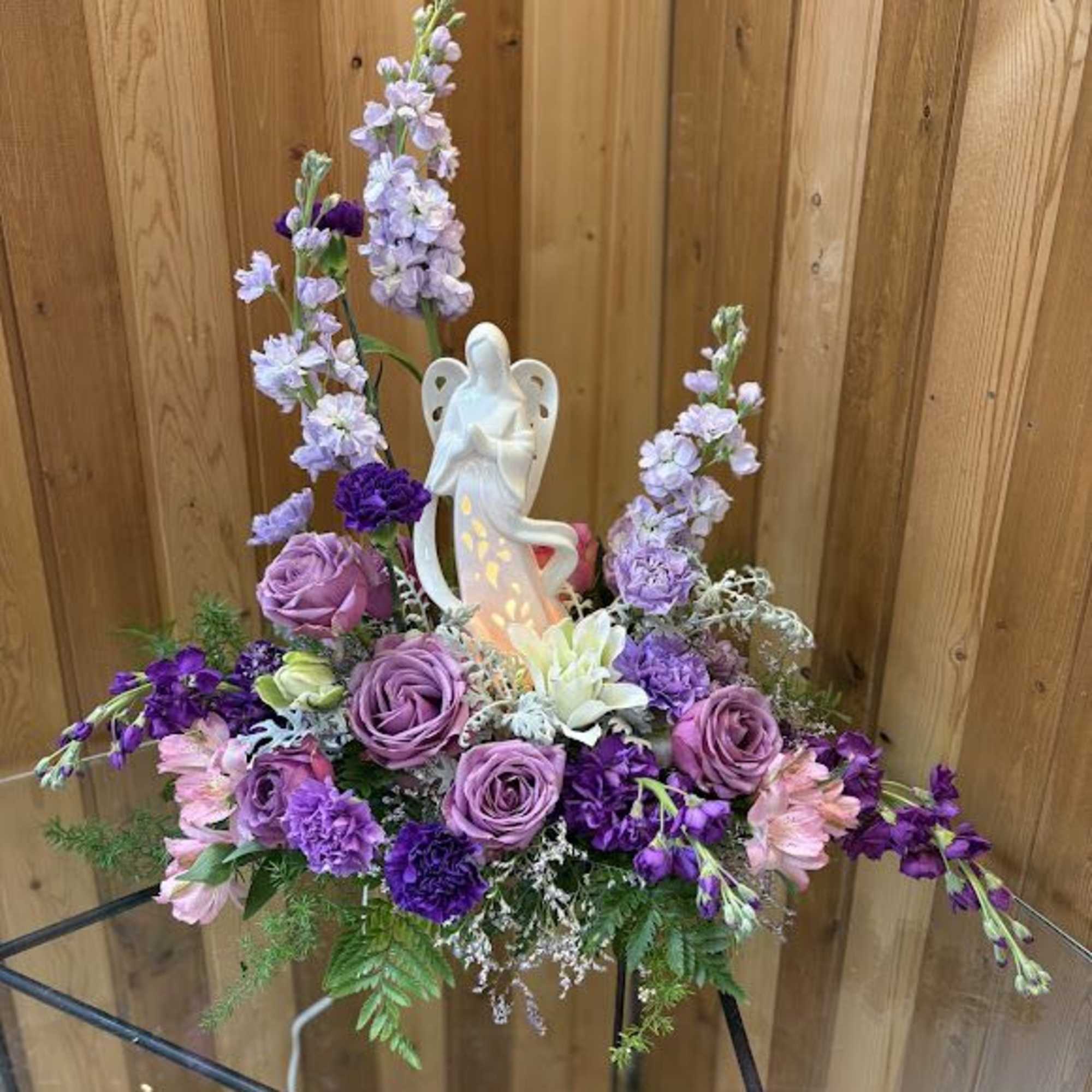 Purple floral arrangement with a white angel figurine centerpiece