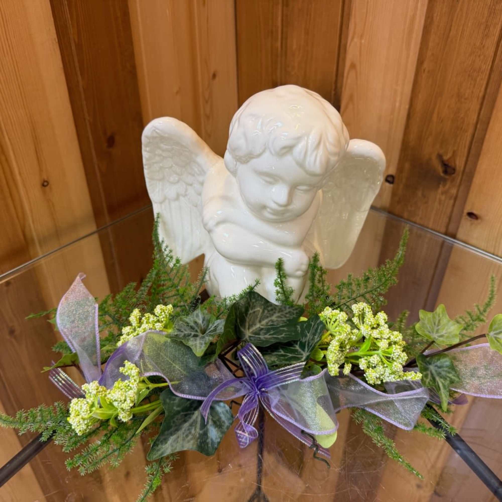 White angel figurine with ivy and small white flowers on a glass table