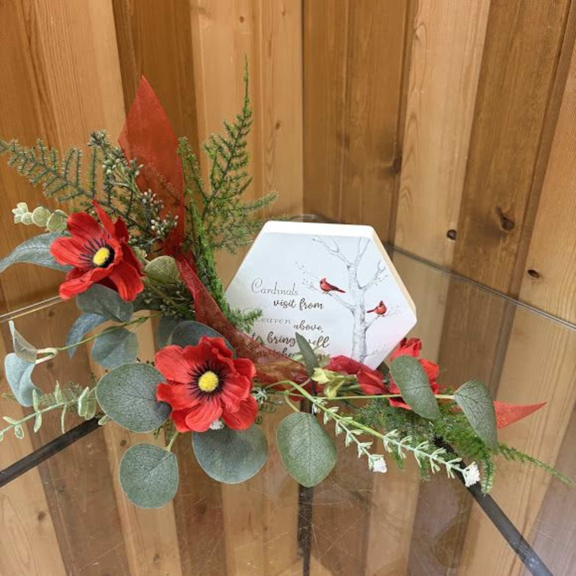 Red flowers and greenery arranged with a cardinal memorial plaque