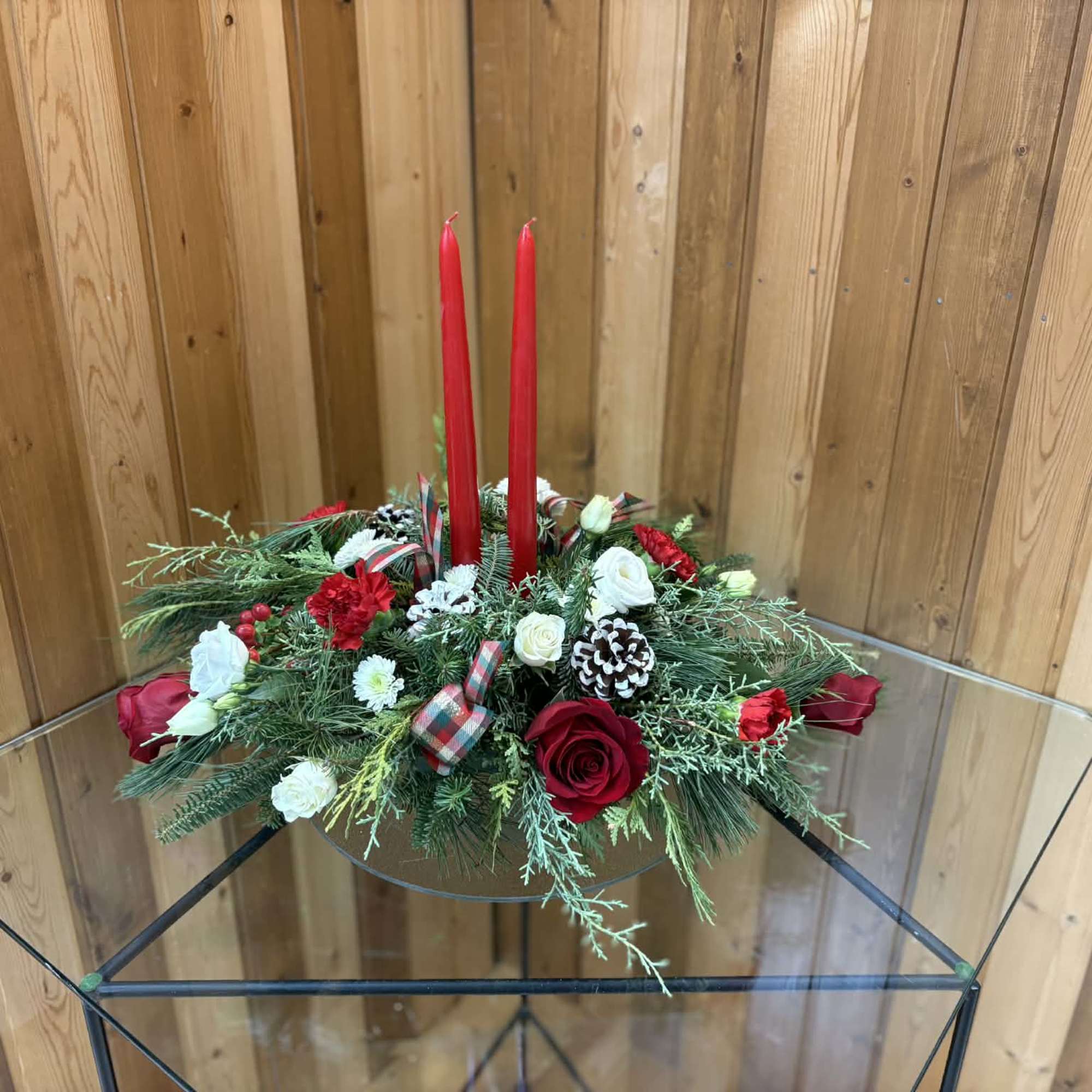 Holiday centerpiece with red candles, roses, and pinecones on a glass table
