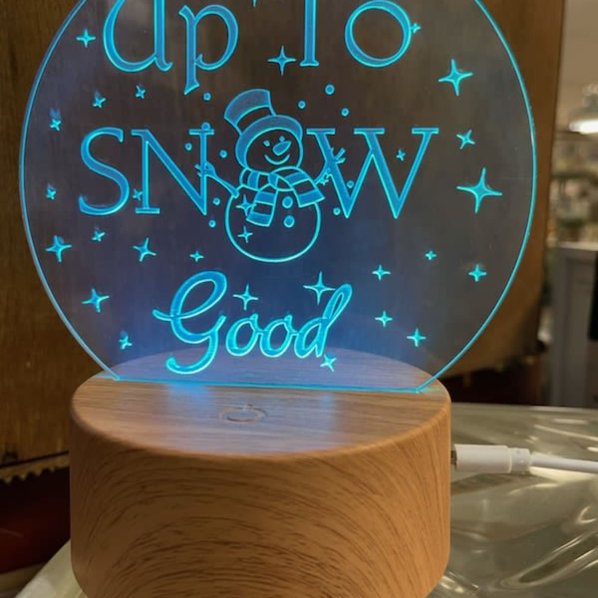 Glowing acrylic sign reading "Up To SNOW Good" on a wood base