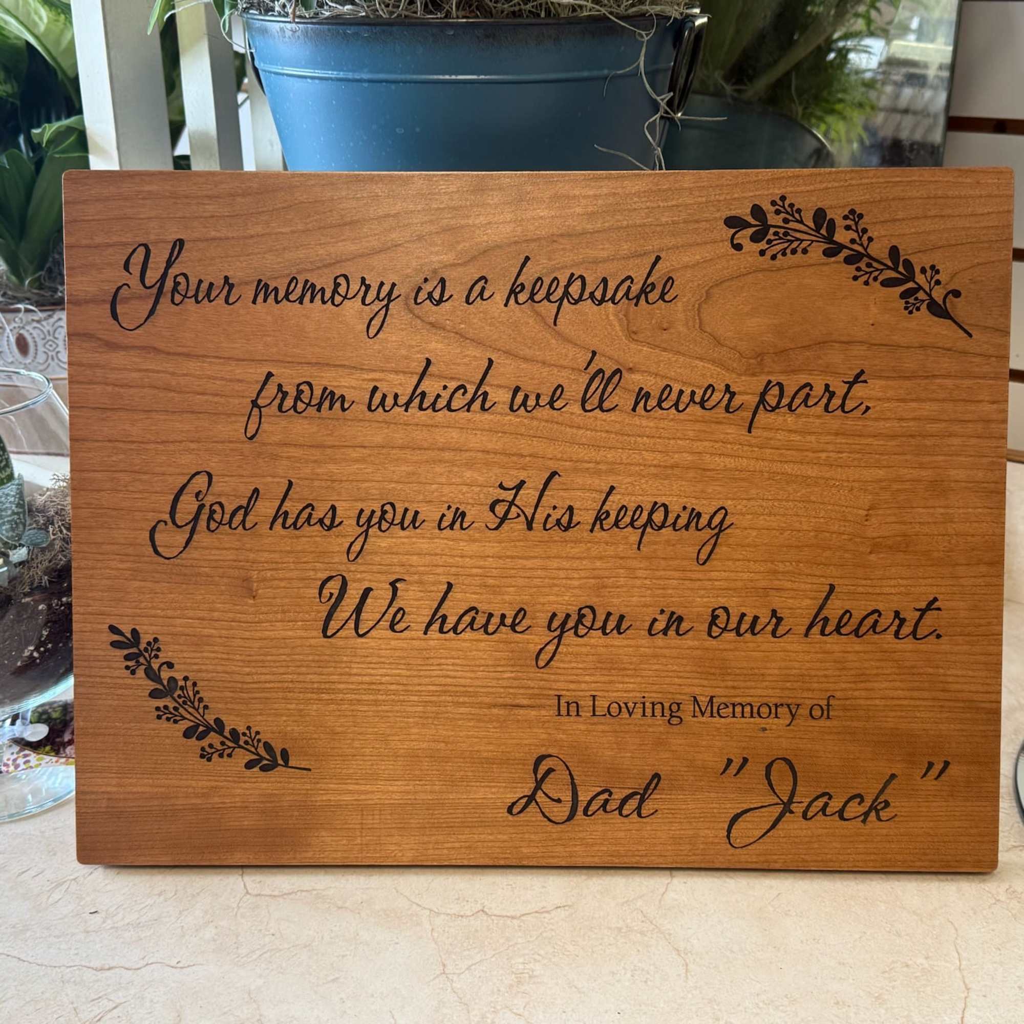 Wood memorial plaque with engraved sympathy message and potted plants nearby