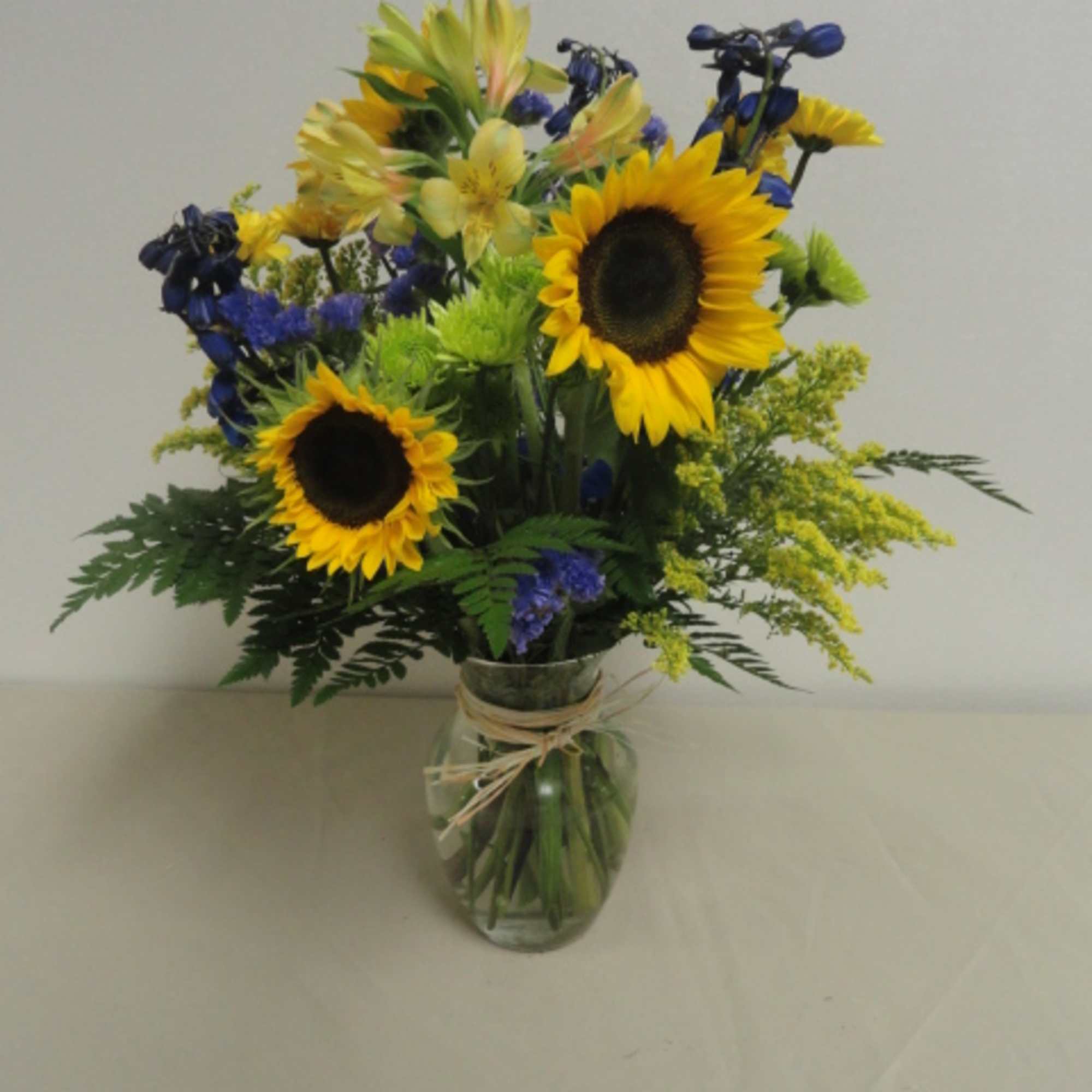 Sunflower bouquet in a clear glass vase with blue and yellow flowers