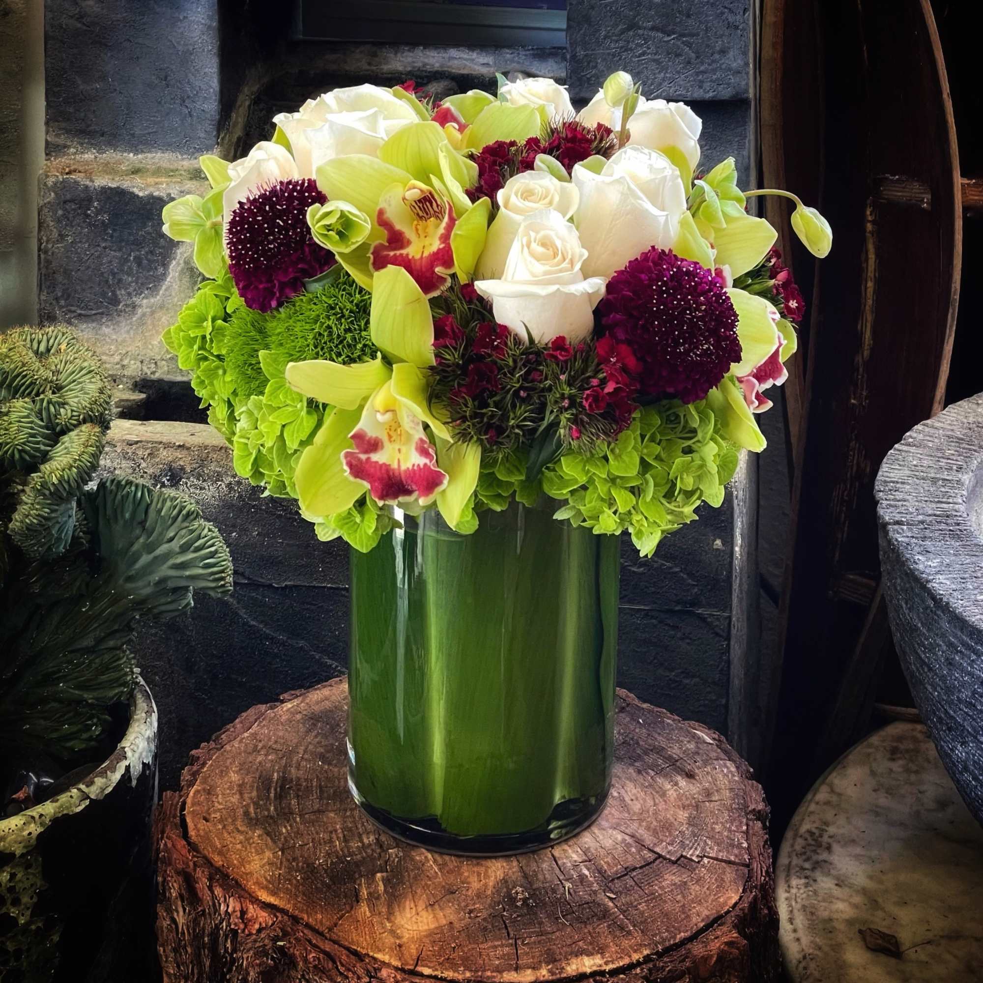 Bouquet of white roses, green orchids, and burgundy blooms in a glass vase