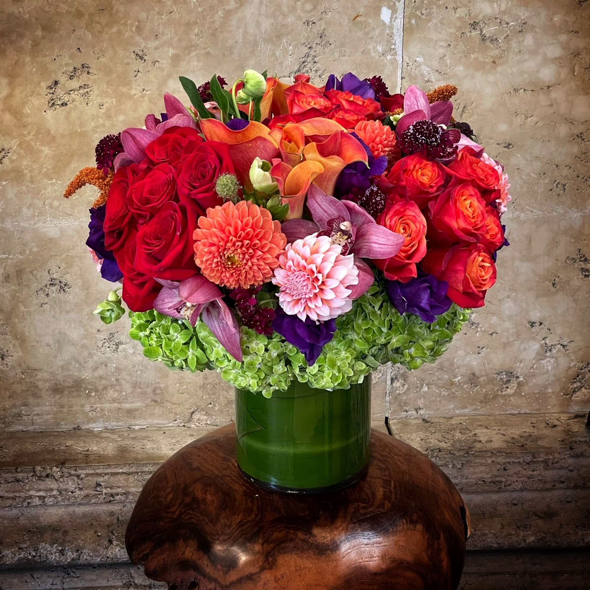 Colorful bouquet of roses, calla lilies, and dahlias in a green vase