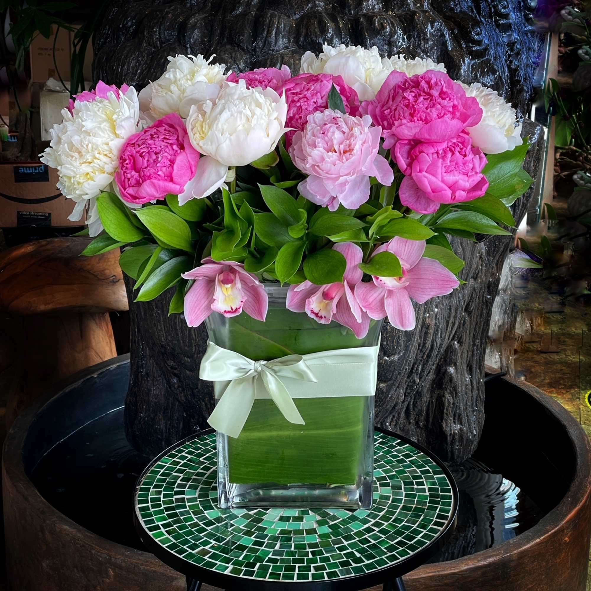 Pink and white peonies in a clear square vase with a ribbon