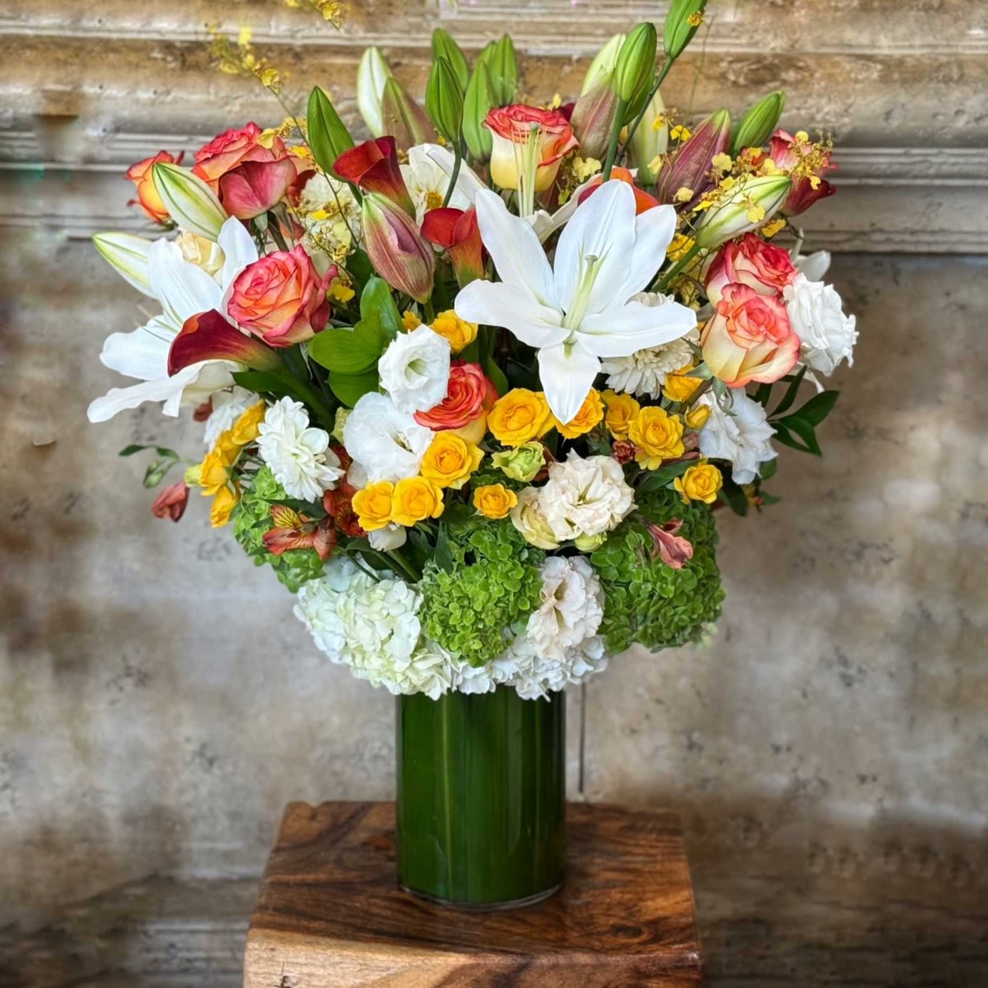 Mixed bouquet of white lilies, roses, and yellow blooms in a green vase