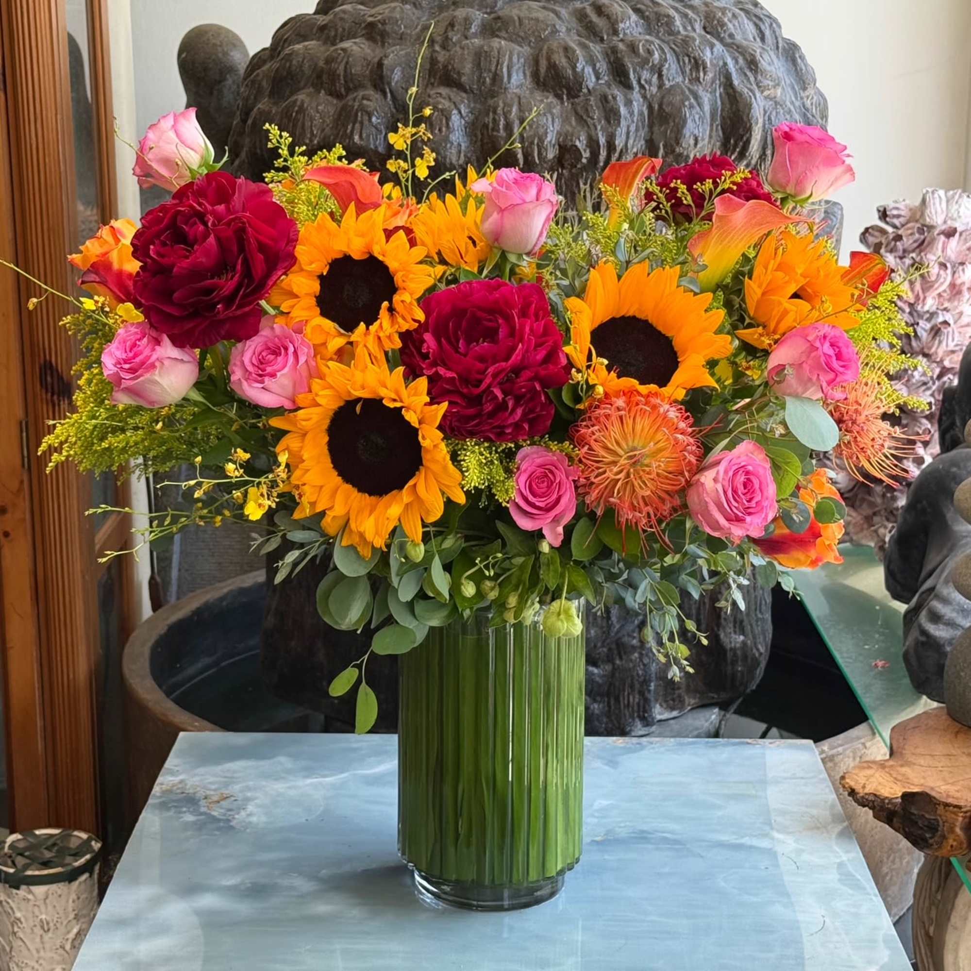 Bright mixed bouquet with sunflowers, roses, and orange blooms in a glass vase