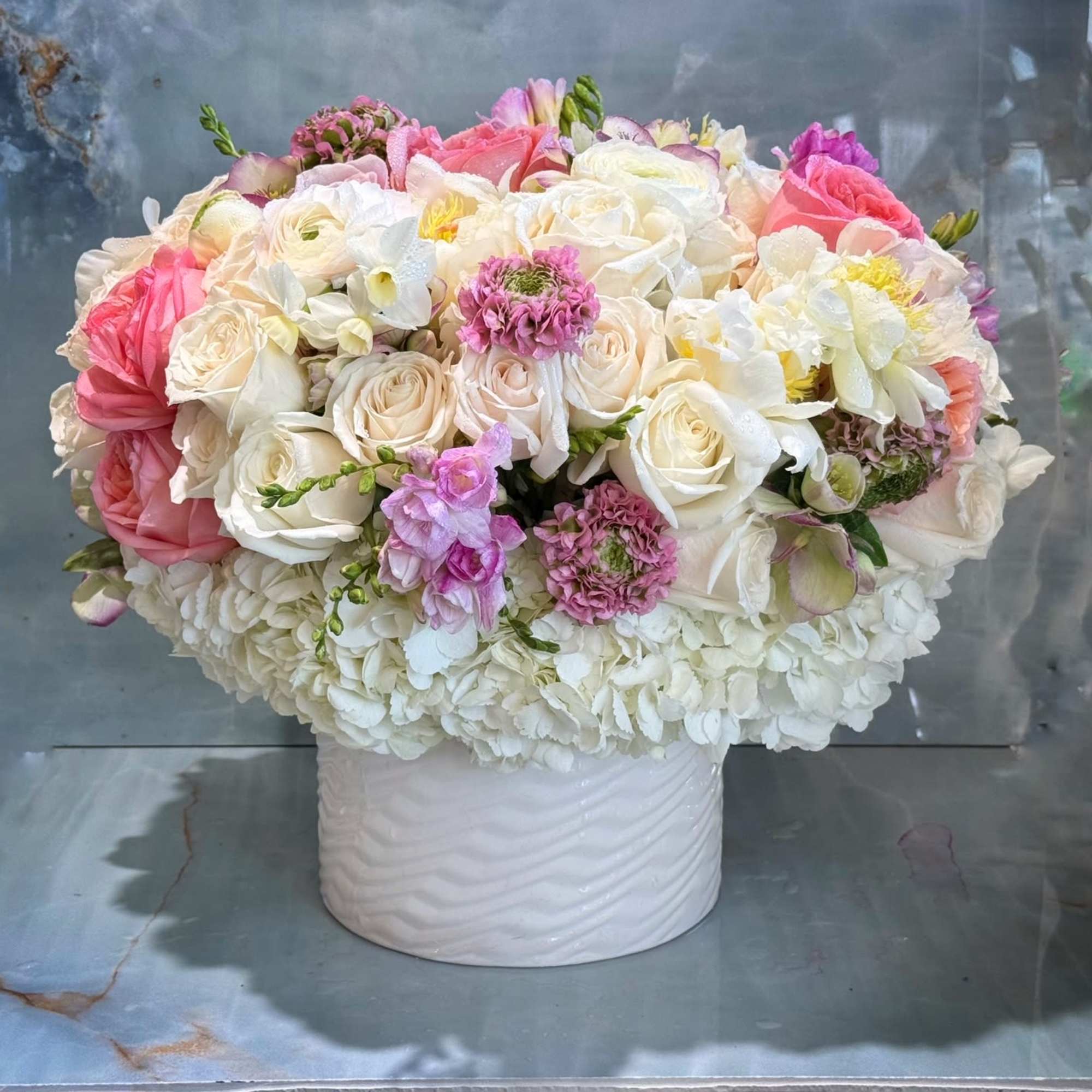 Low round arrangement of white and pink flowers in a white ceramic cylinder vase