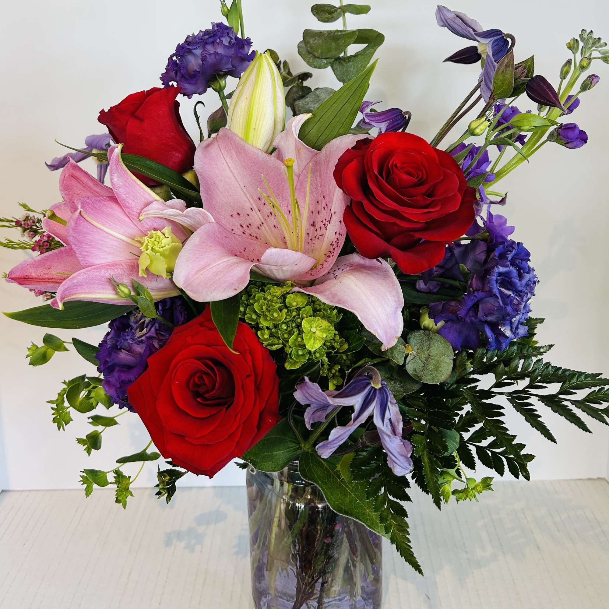 Bouquet of red roses, pink lilies, and purple flowers in a glass vase