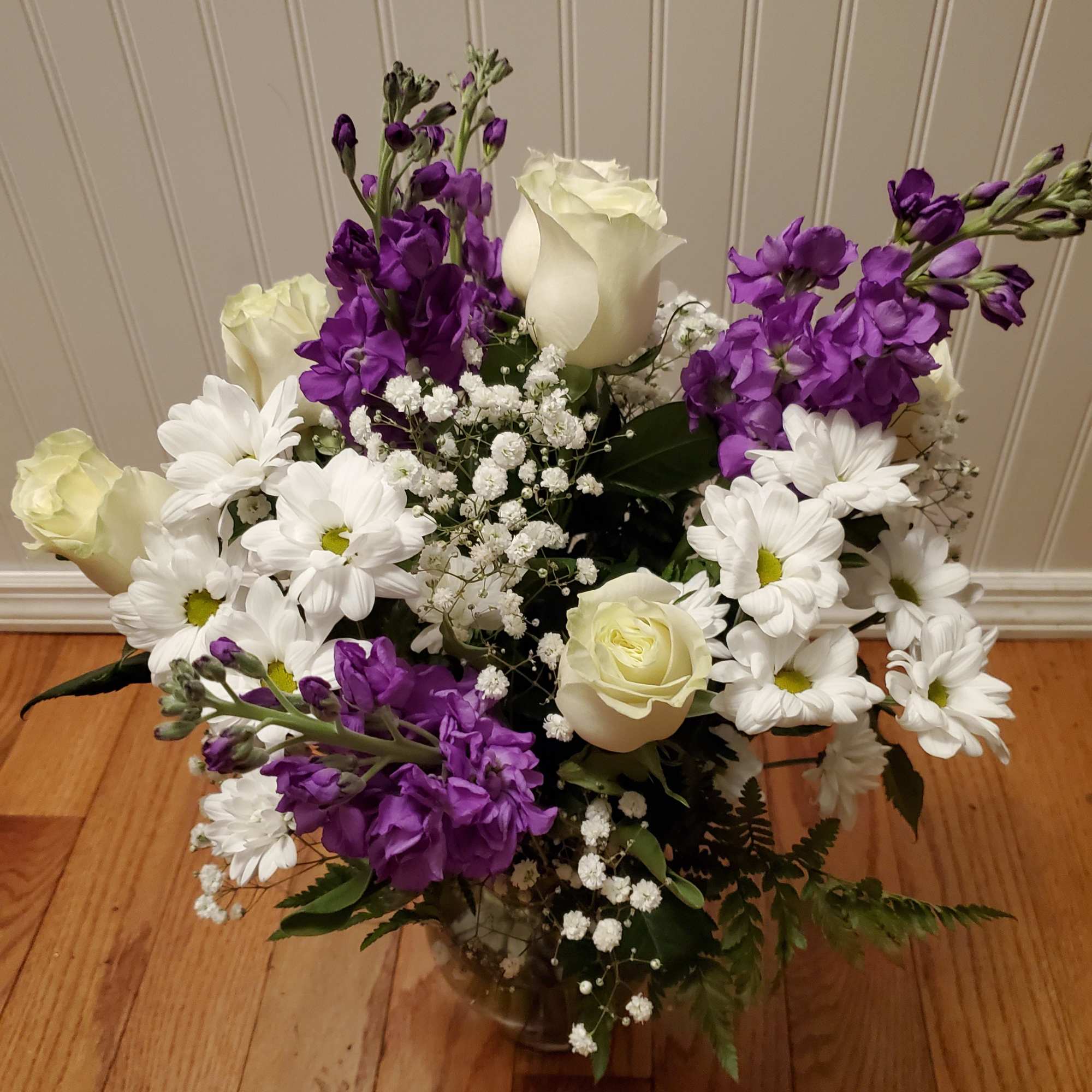 Mixed bouquet of white roses, white daisies, and purple flowers arranged in a clear glass vase