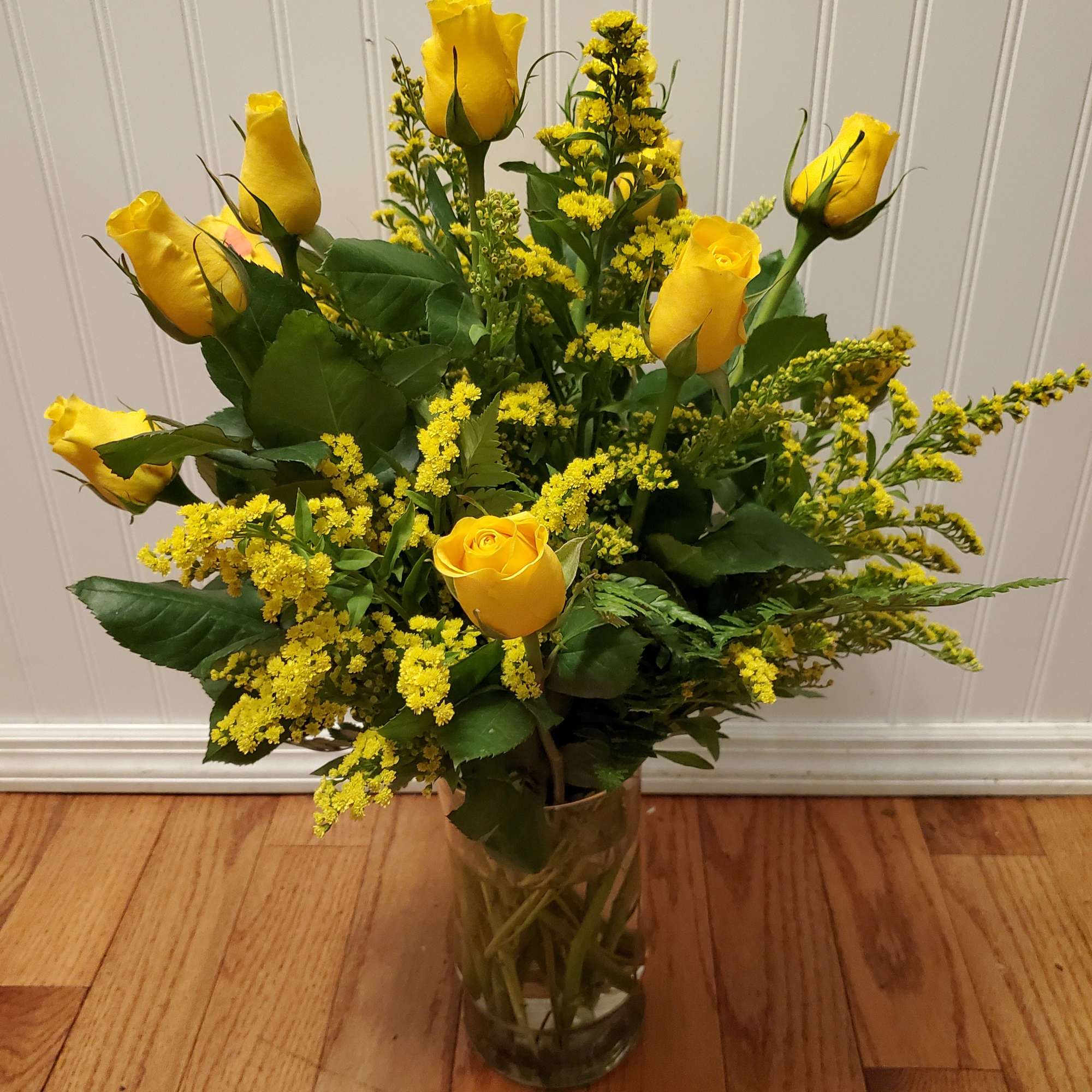 Tall arrangement of yellow roses with yellow filler in a clear glass vase