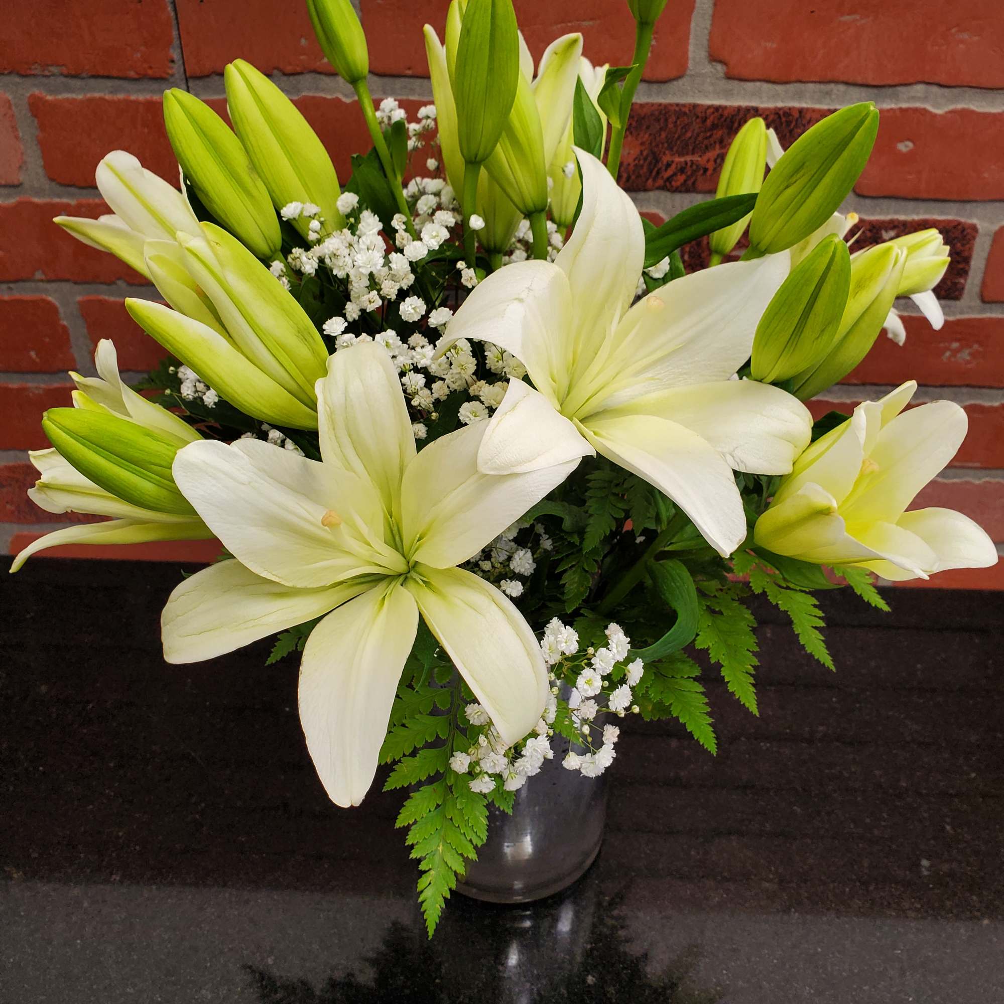 Arrangement of white lilies with buds and small white filler flowers in a silver vase
