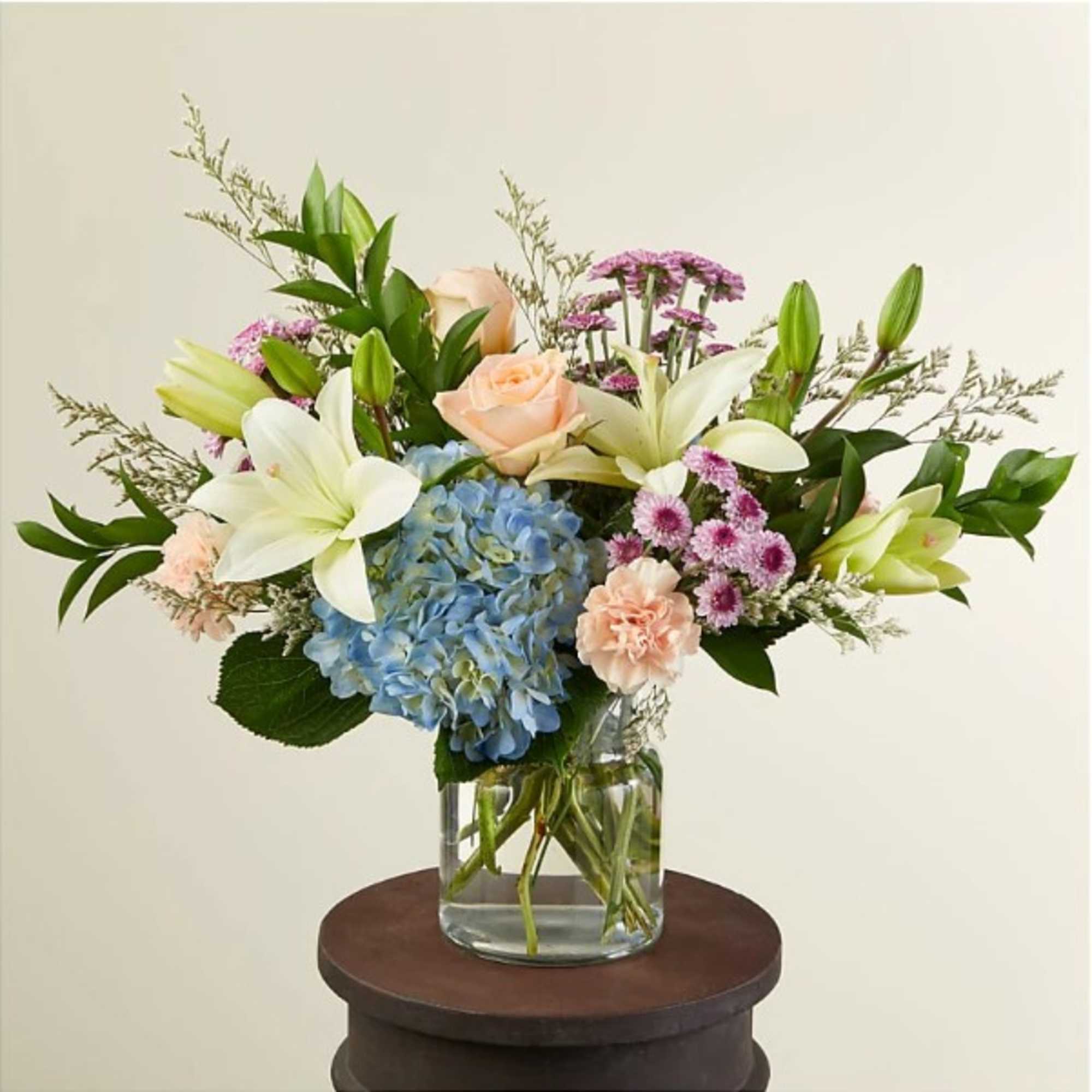 Mixed bouquet of white lilies, peach roses, blue hydrangea and pink blooms in a clear glass vase