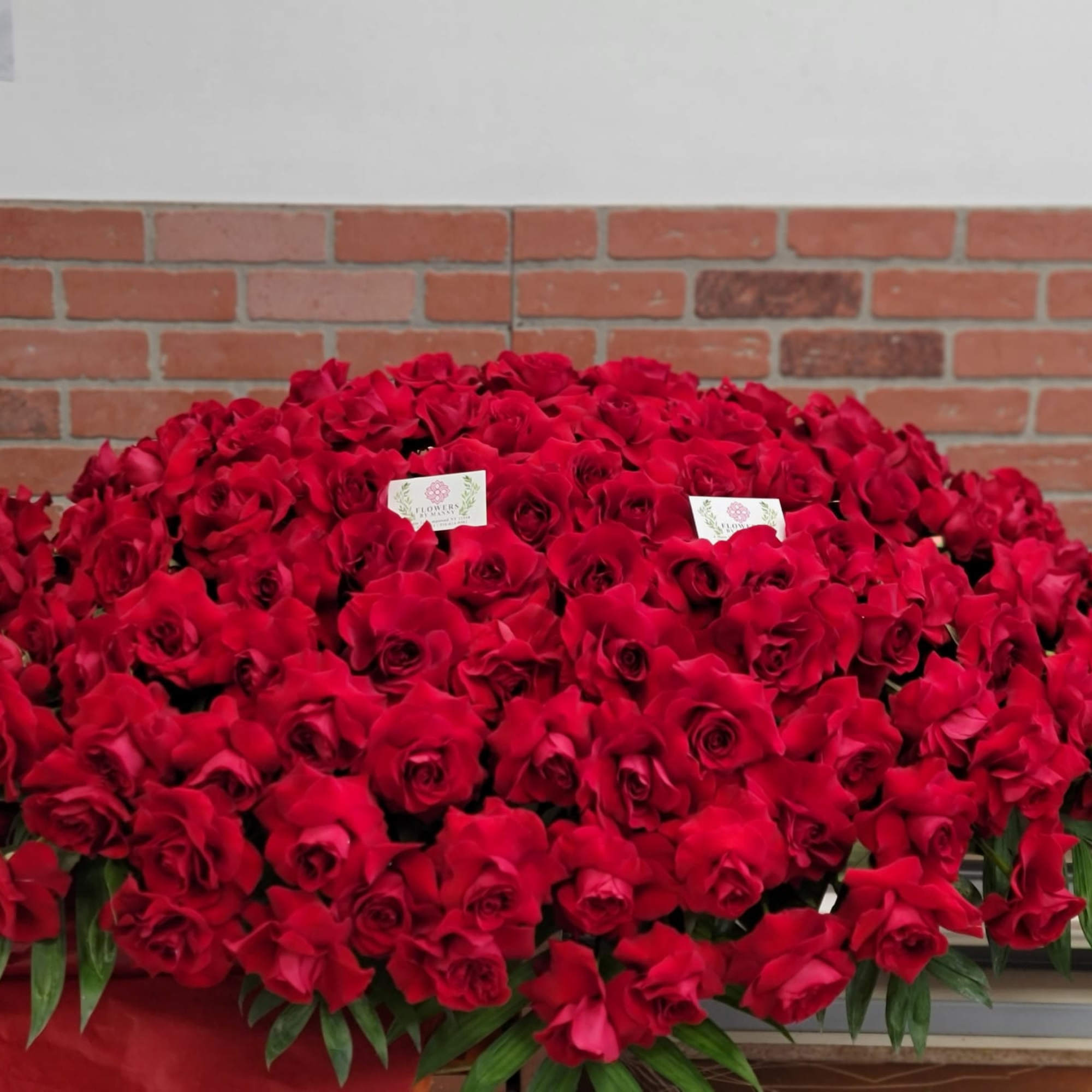 Large mound of red roses arranged in a dense casket spray with a few cards tucked among the blooms