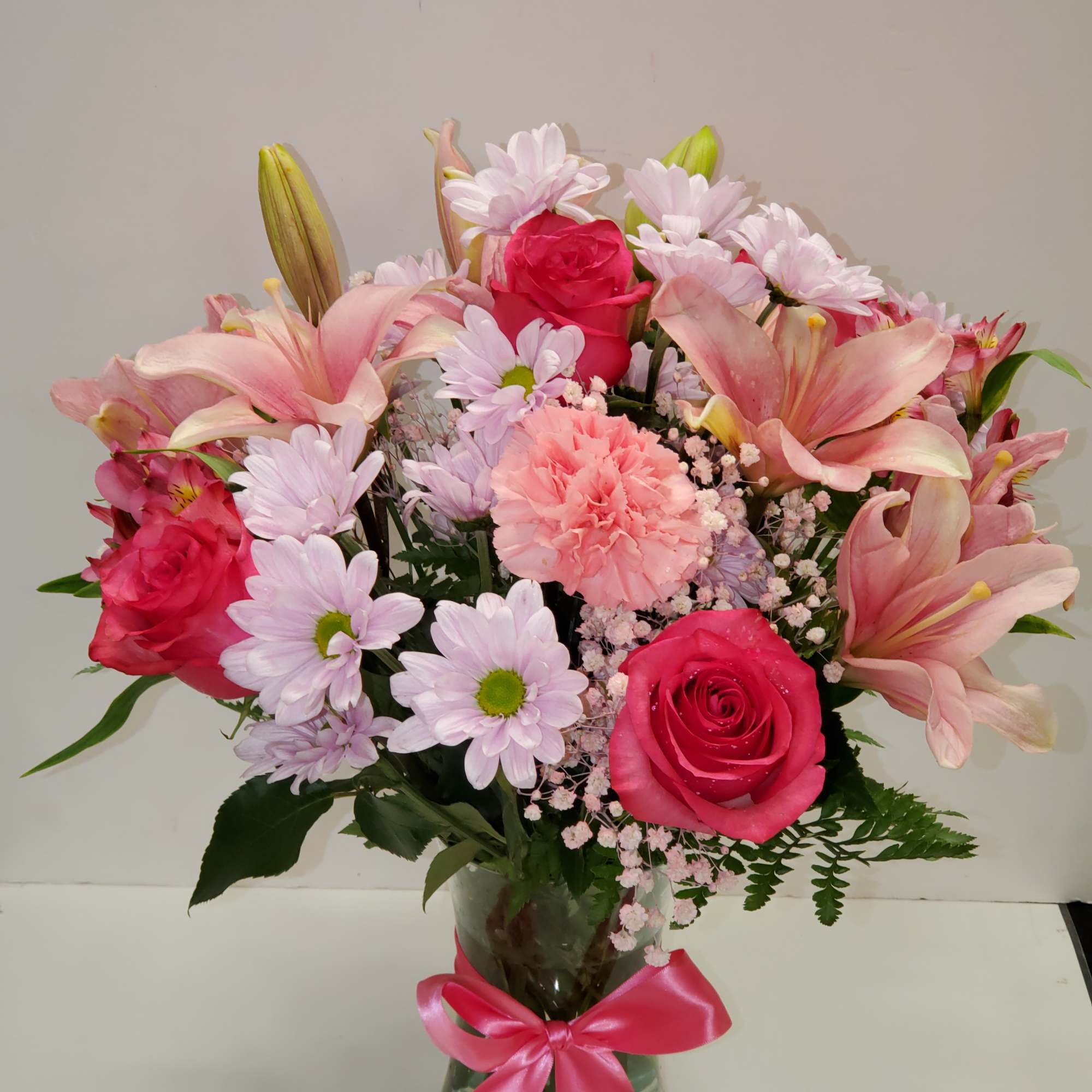 Vase arrangement of pink roses, lilies, daisies, and a carnation with a pink bow