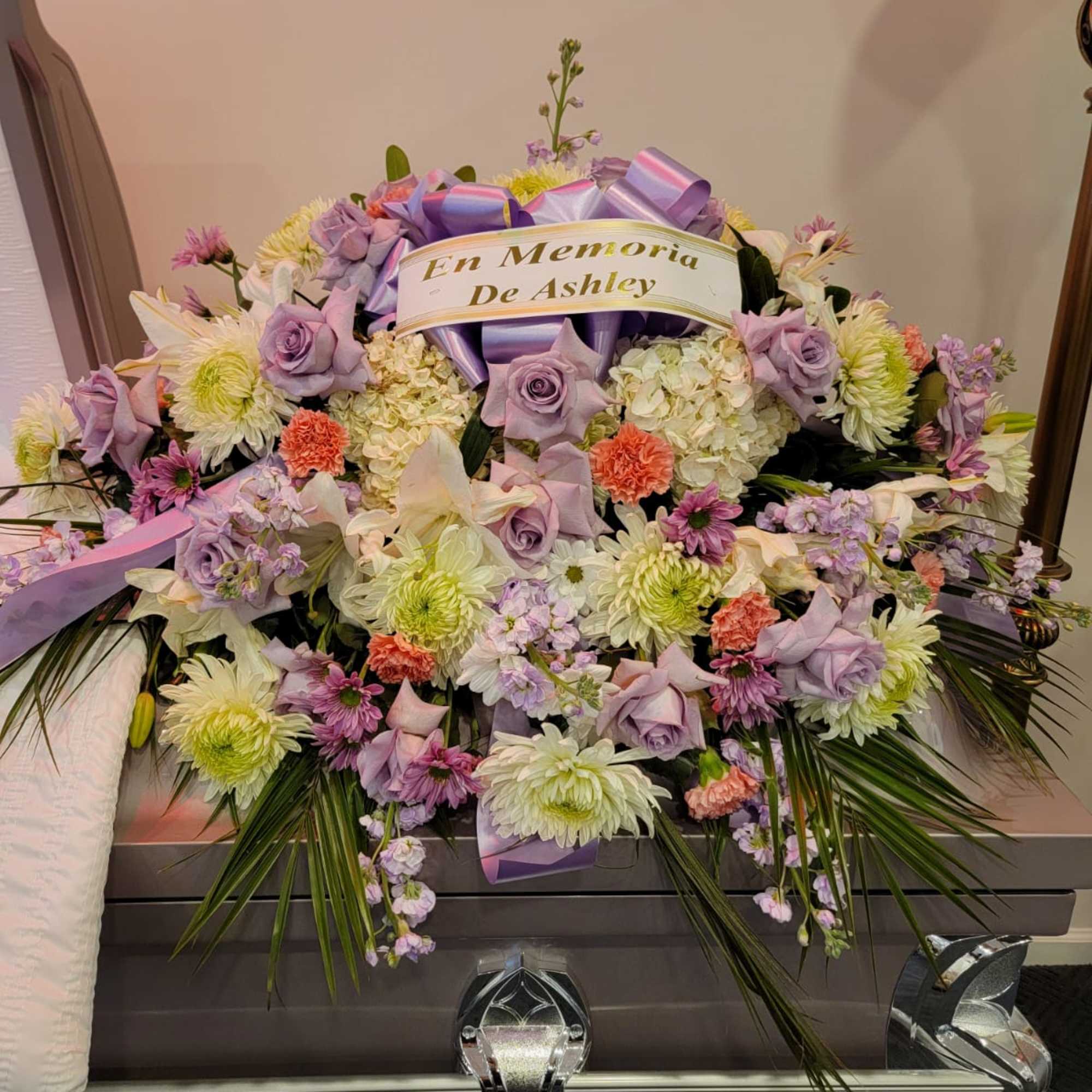 Casket spray of lavender roses, white mums, and mixed blooms with a memorial ribbon