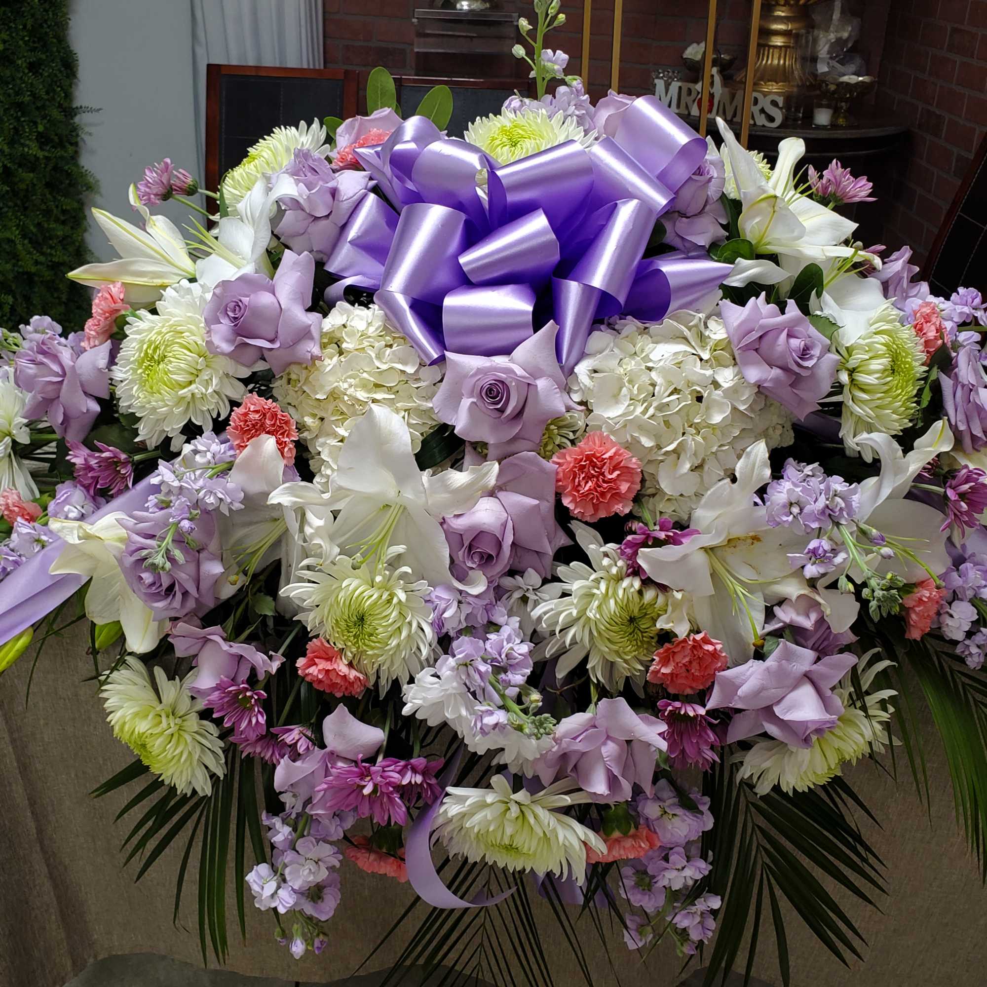 Large pastel casket spray with lavender roses, white lilies, mums, carnations, and a lavender bow