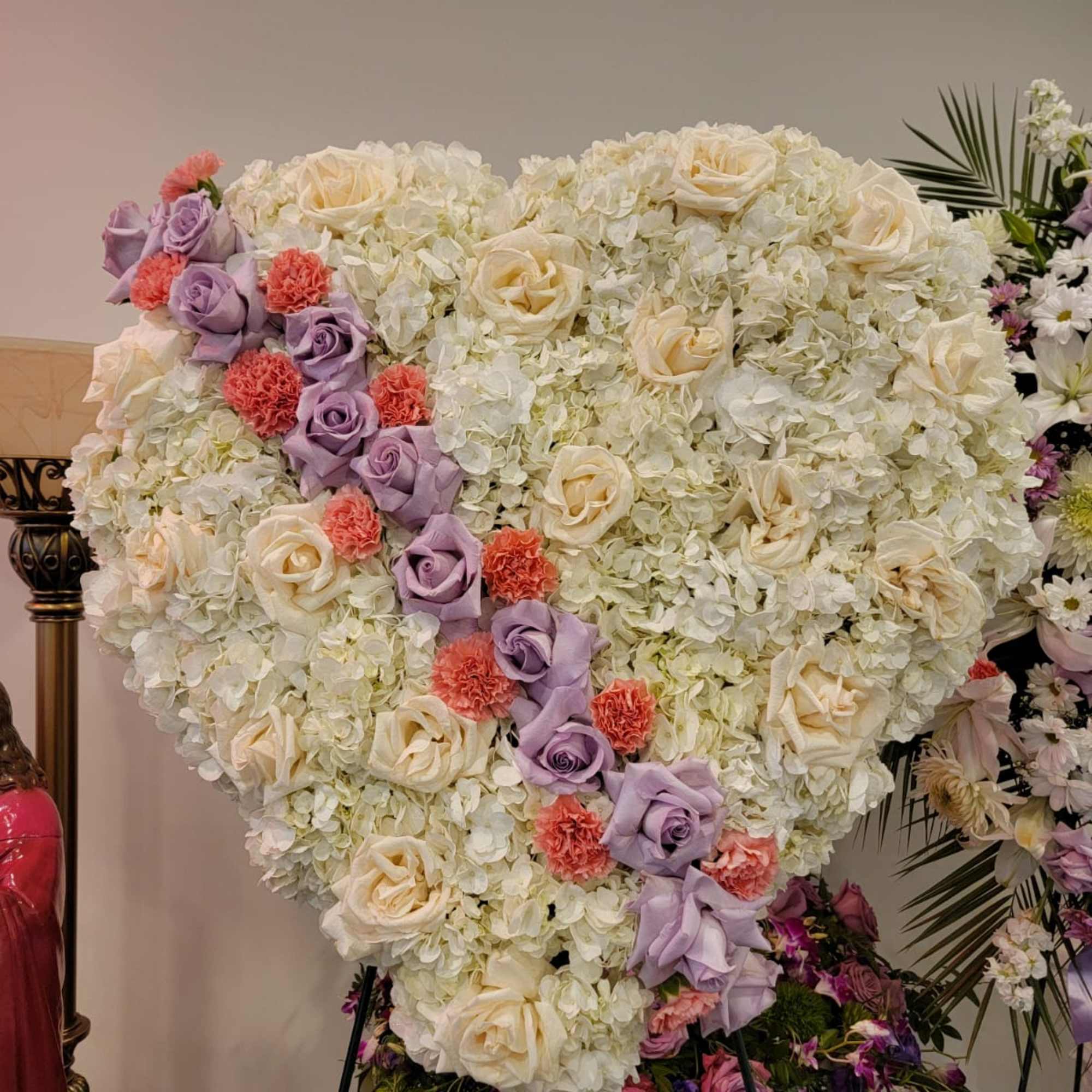 Large heart-shaped standing arrangement of white flowers with lavender roses and coral carnations on an easel