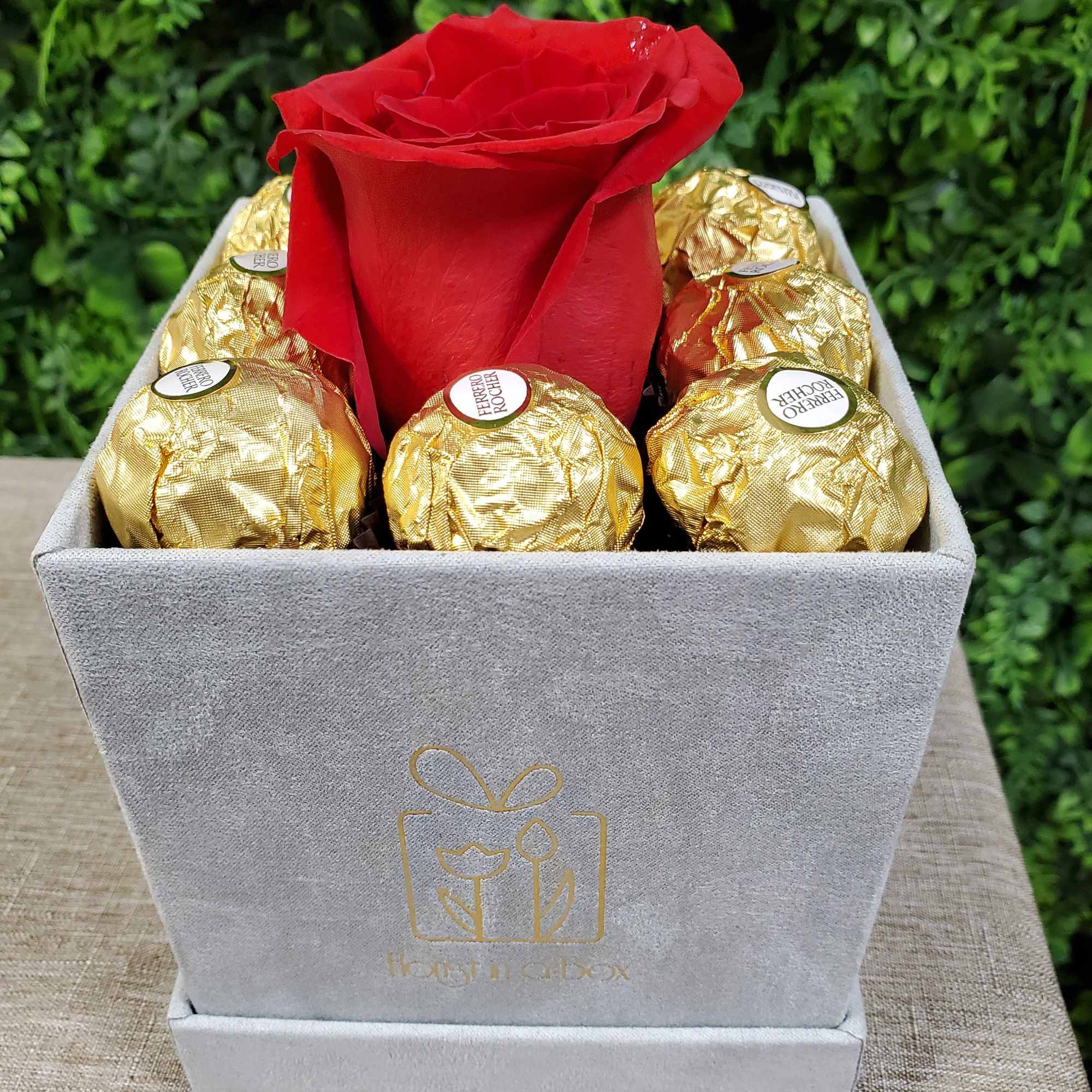 Gray velvet box with a single red rose surrounded by gold-wrapped chocolates