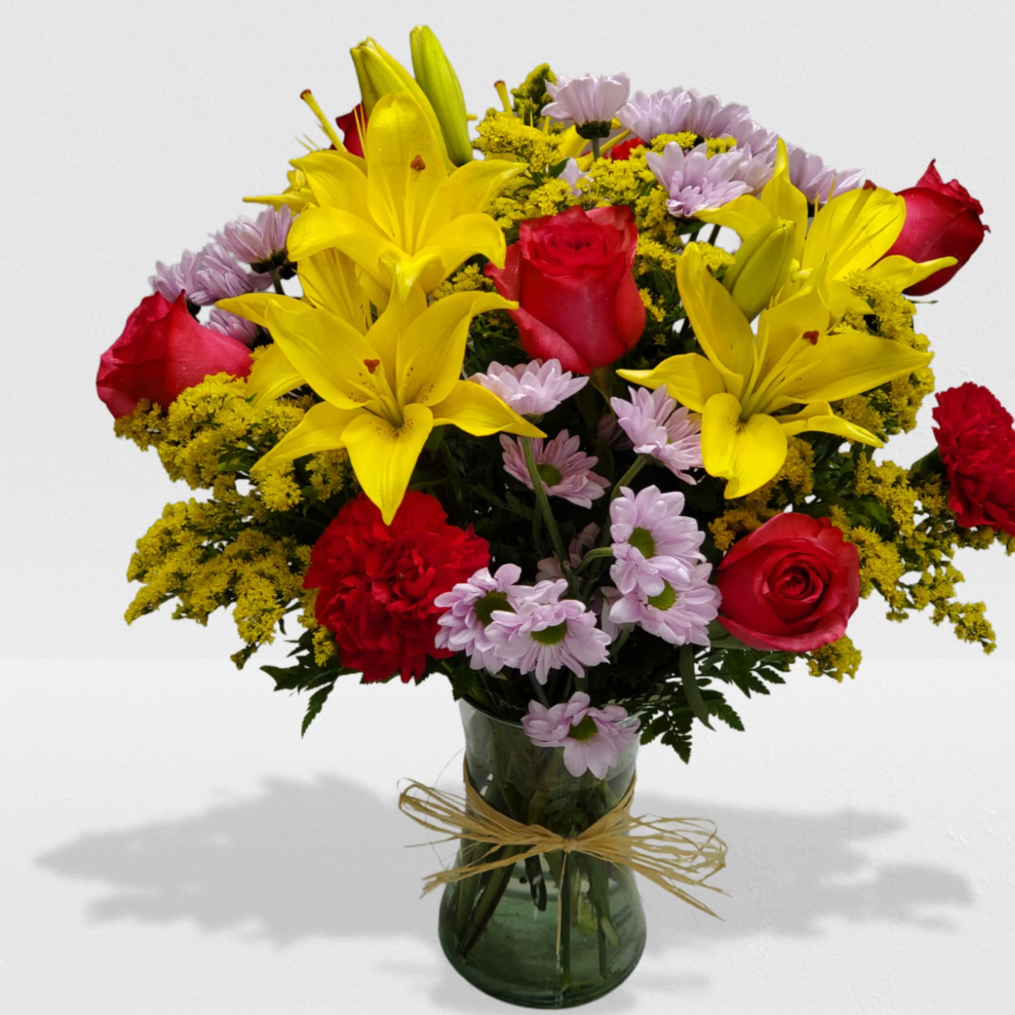 Mixed bouquet of yellow lilies, red roses, and daisies in a green glass vase with raffia bow