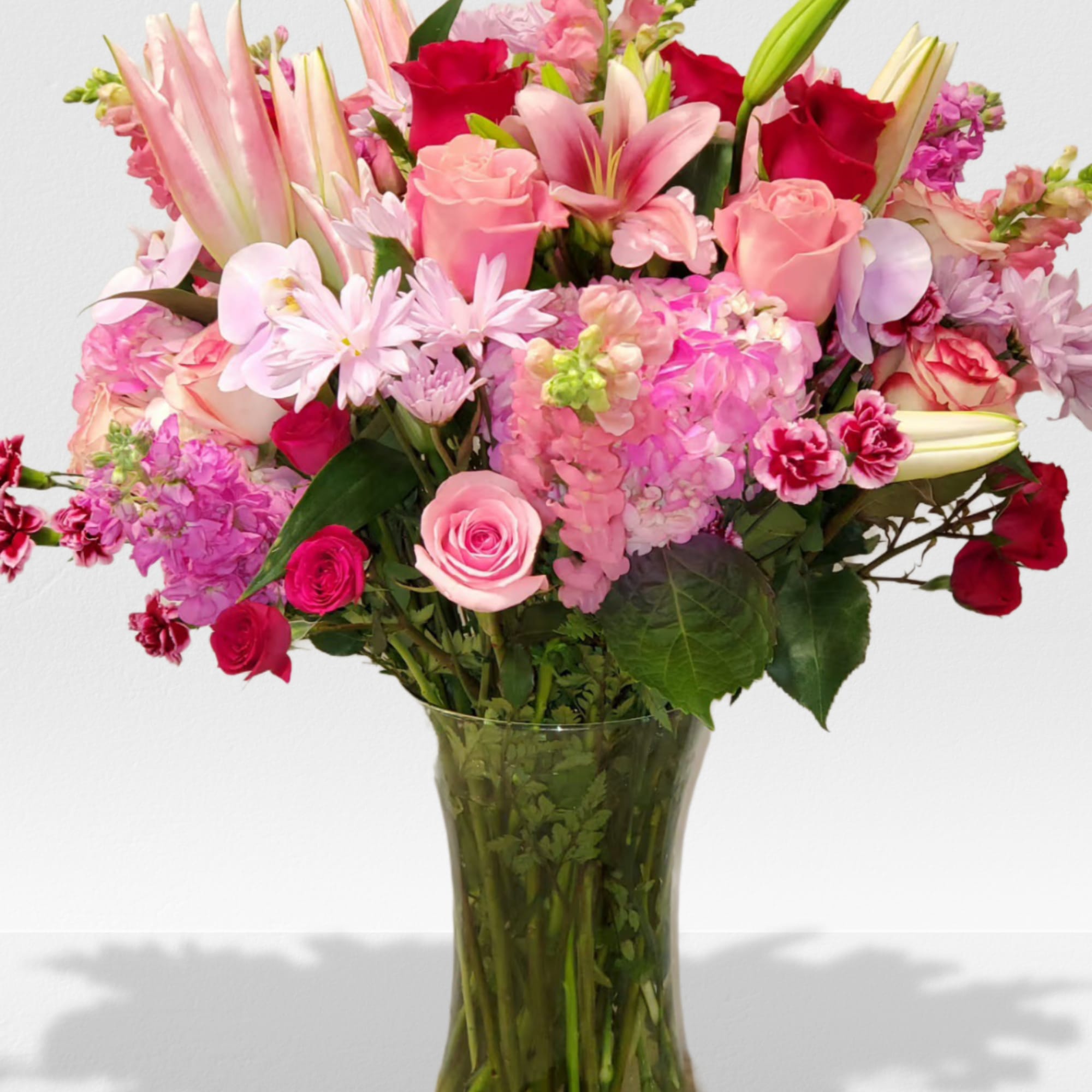 Tall glass vase of pink and red roses, lilies, snapdragons, and mixed flowers