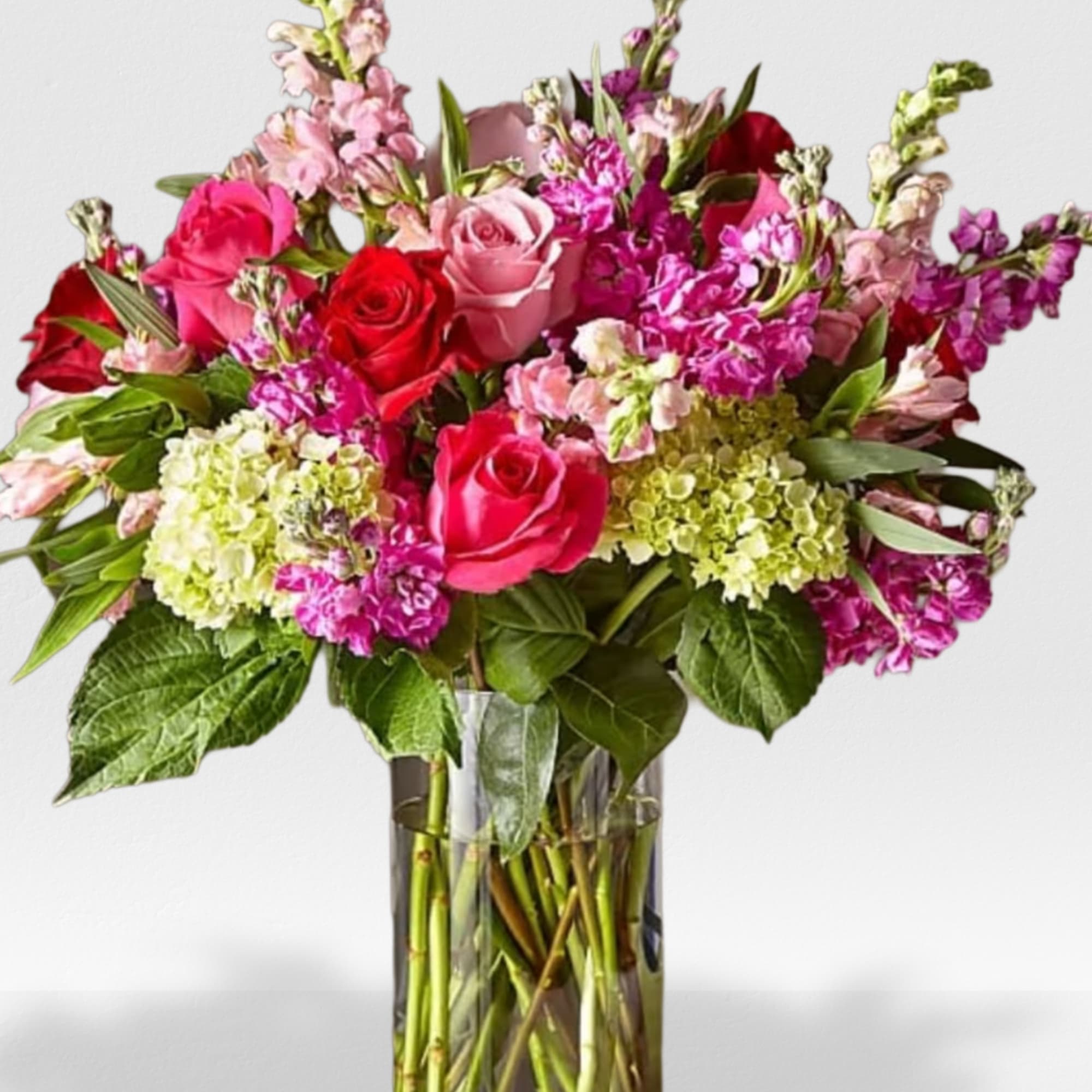 Tall arrangement of pink and red roses, pink snapdragons, and green hydrangeas in a glass vase