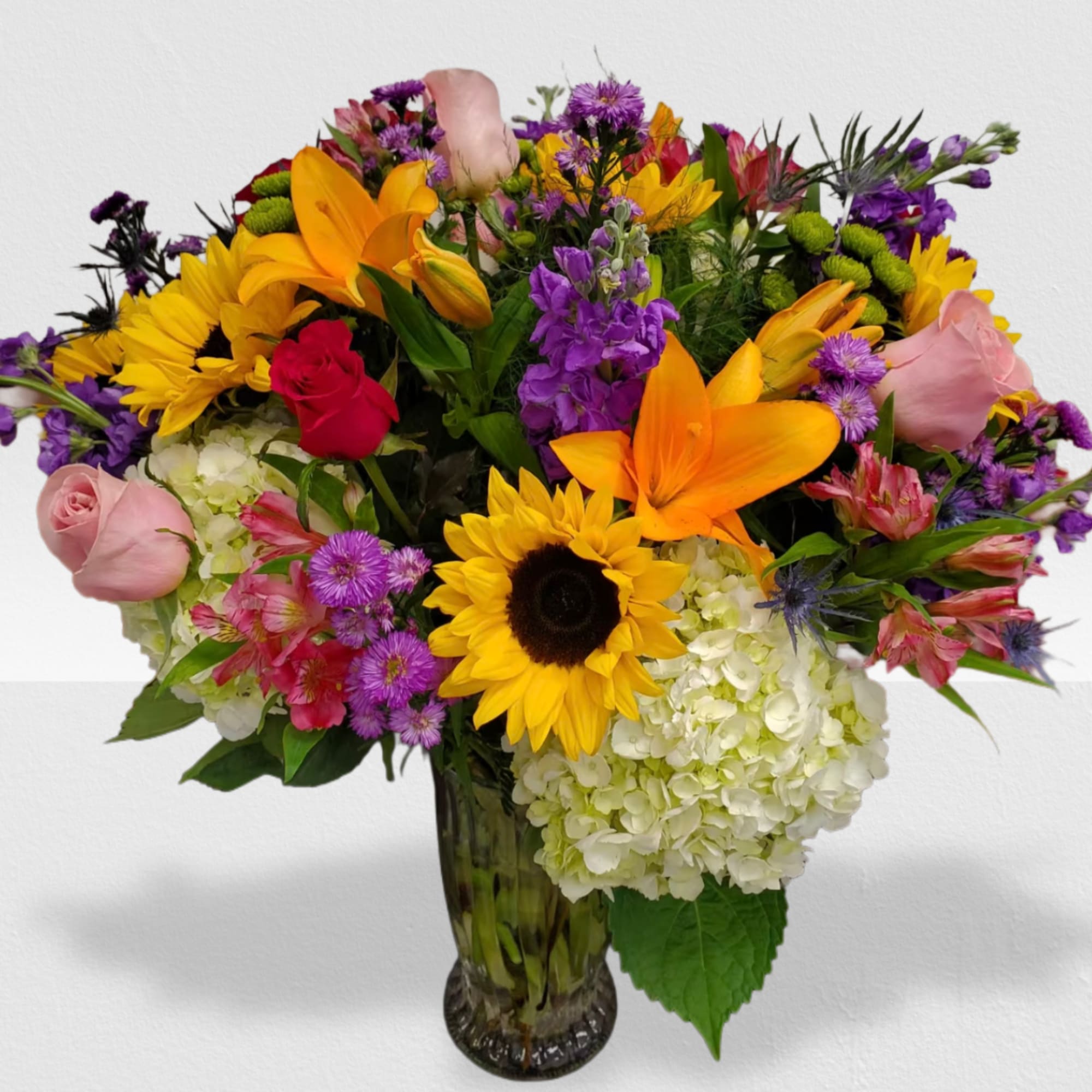 Mixed bouquet of sunflowers, lilies, roses, and hydrangeas in a clear glass vase