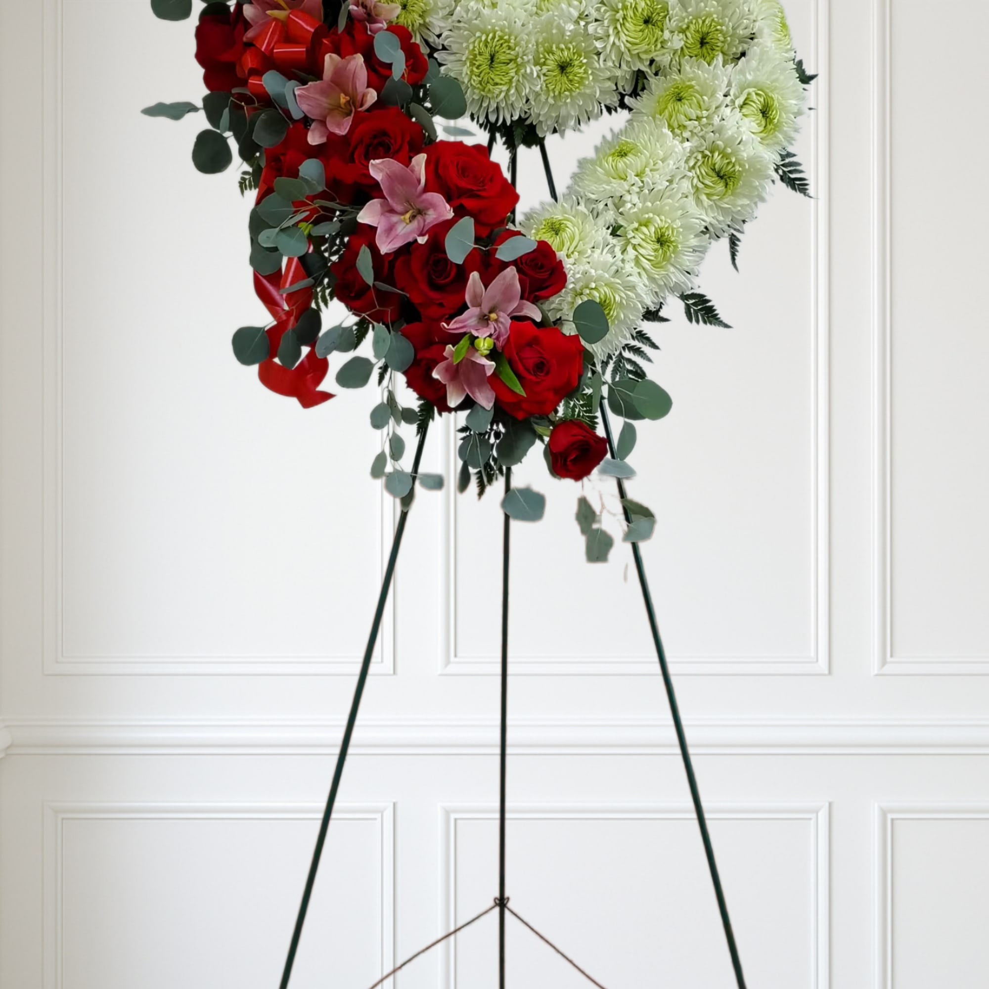 Standing heart of white mums with red roses and pink lilies on an easel with red bows