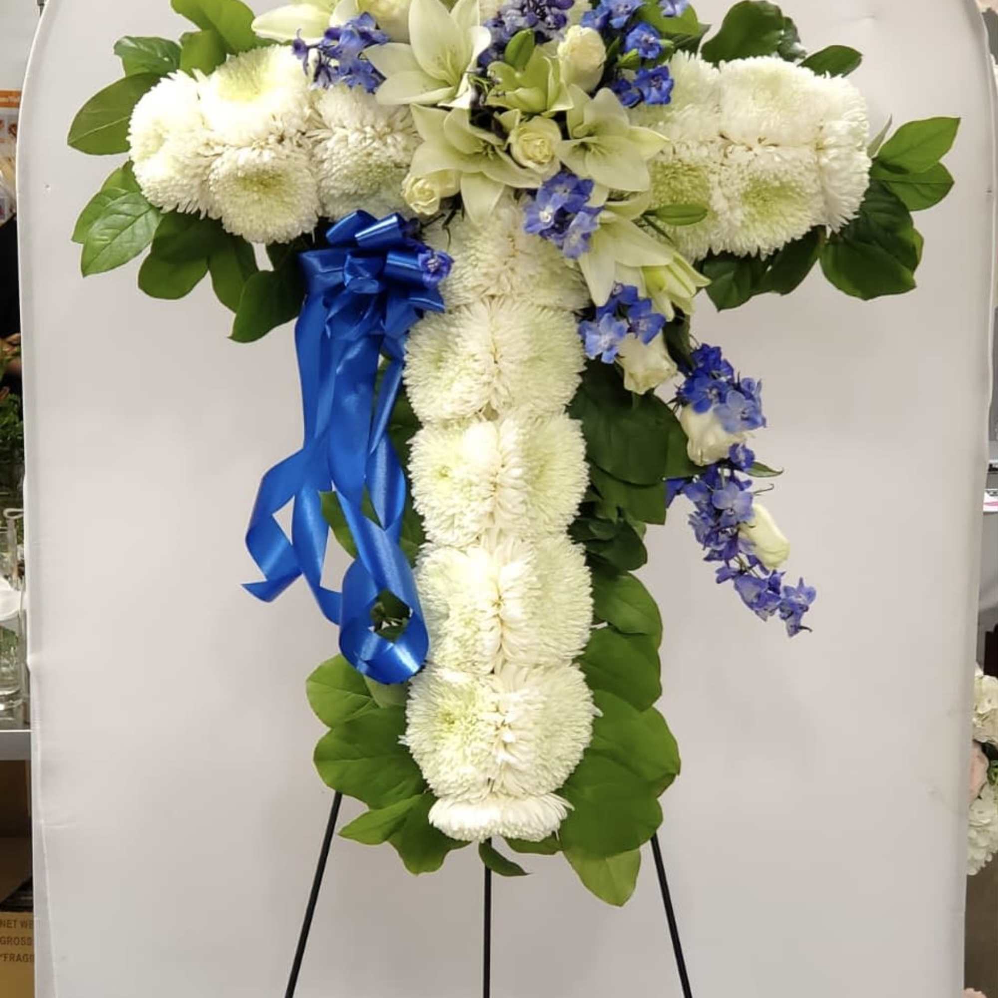 White floral cross on an easel with blue ribbon accents