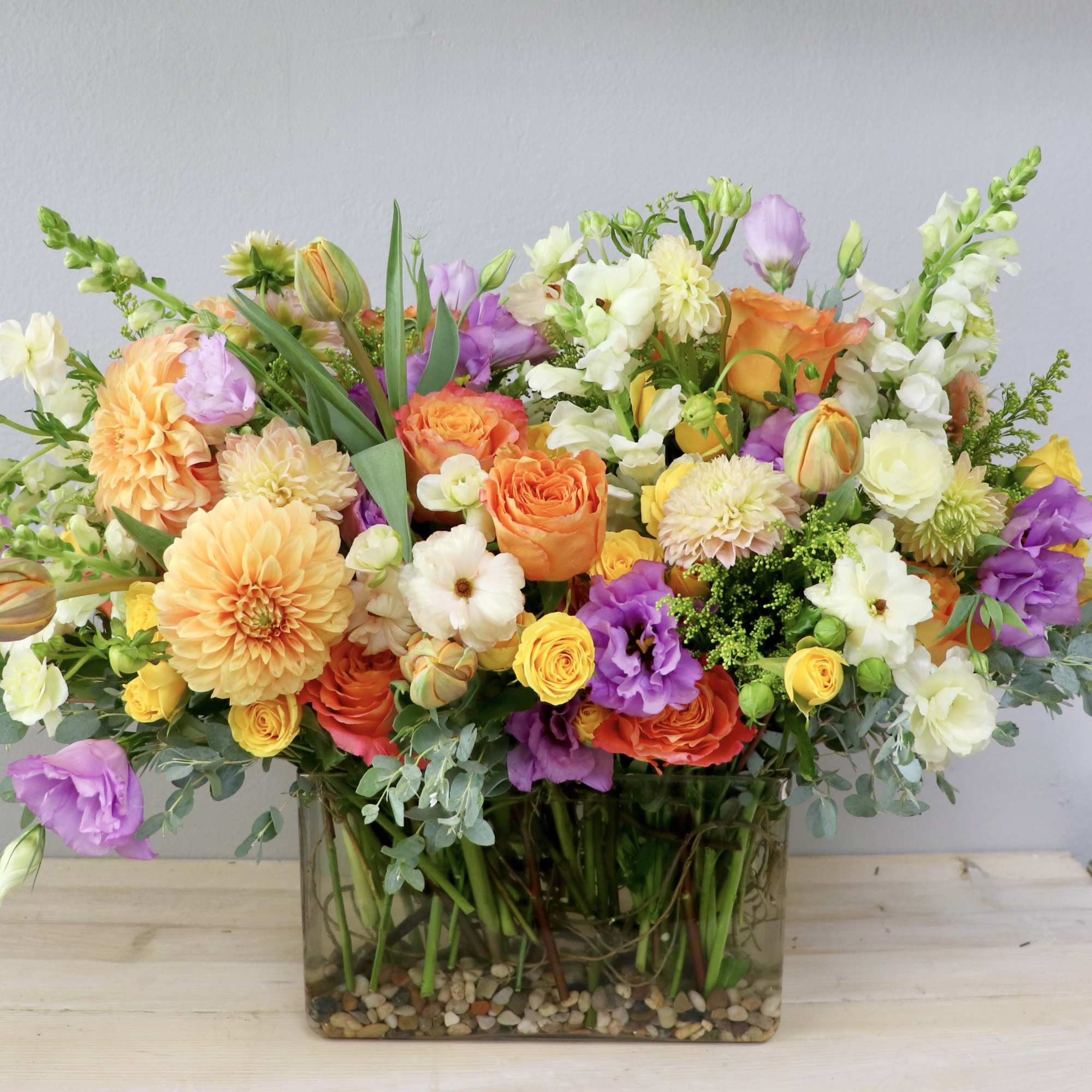 Mixed bouquet of orange, yellow, white, and purple flowers in a glass vase