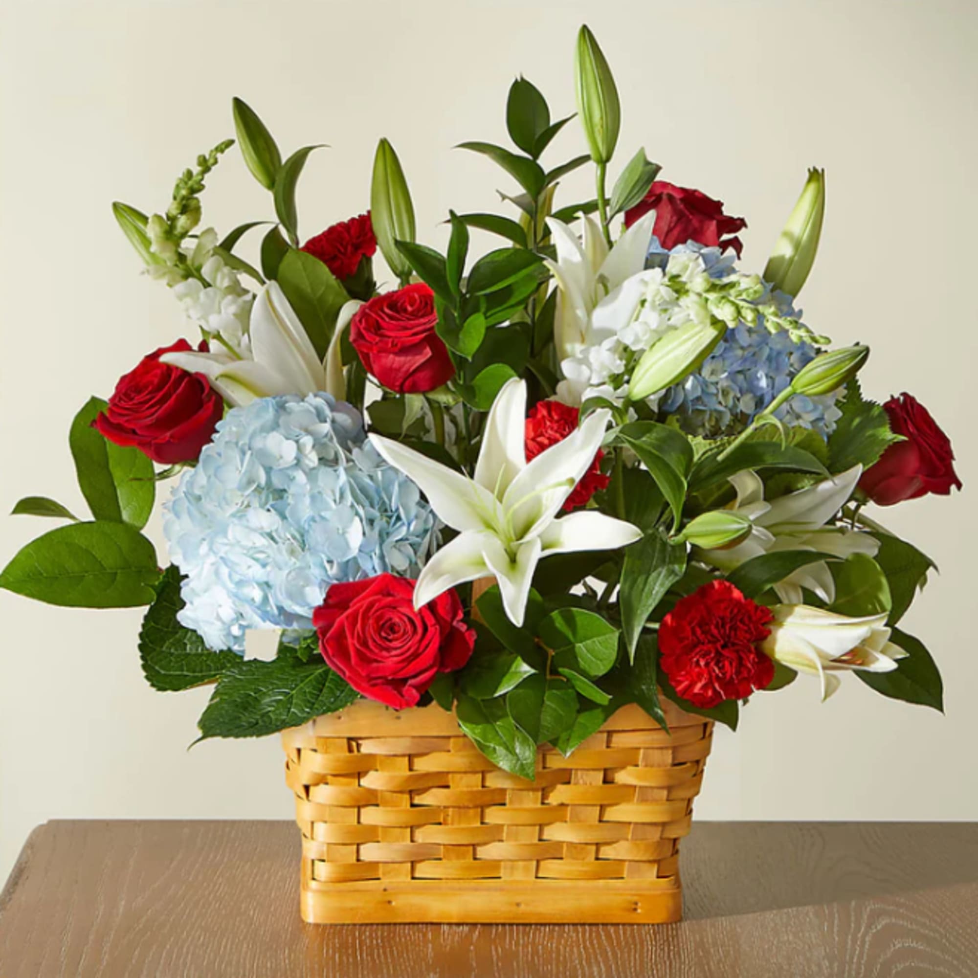 Basket arrangement of red roses, blue hydrangeas, white lilies, and carnations