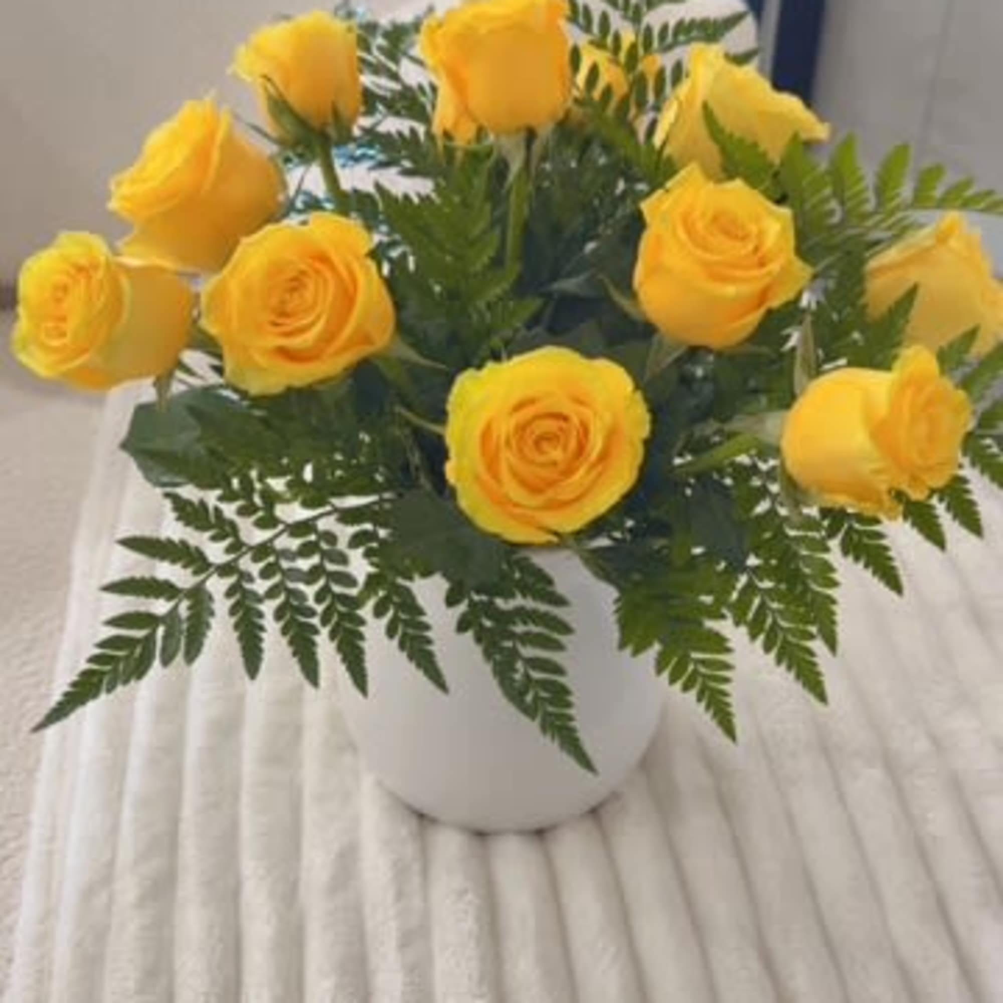 Yellow roses arranged in a white vase with fern foliage