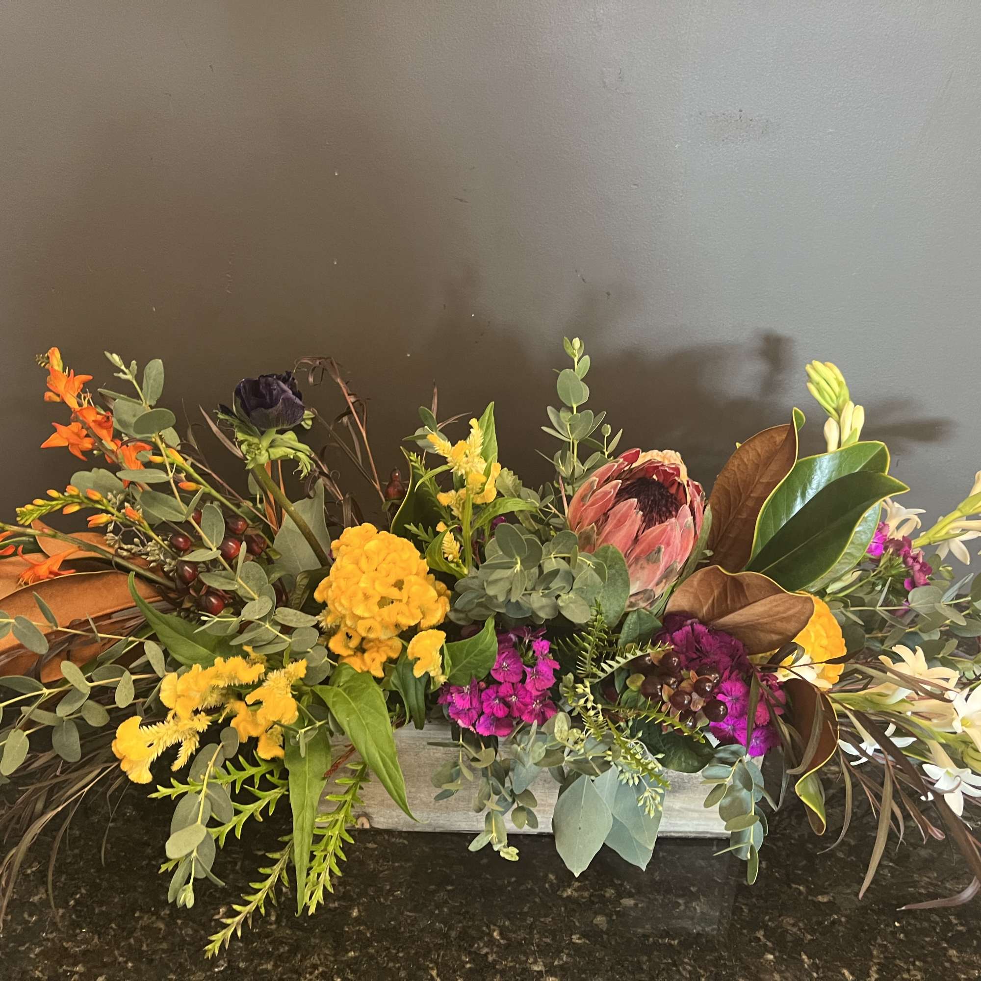Long low floral arrangement with orange, yellow, pink, and white blooms in a rectangular container