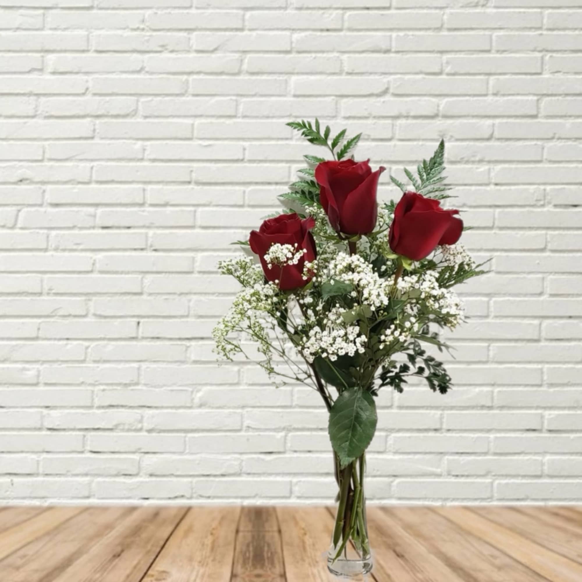Three red roses in a clear glass vase with white filler flowers