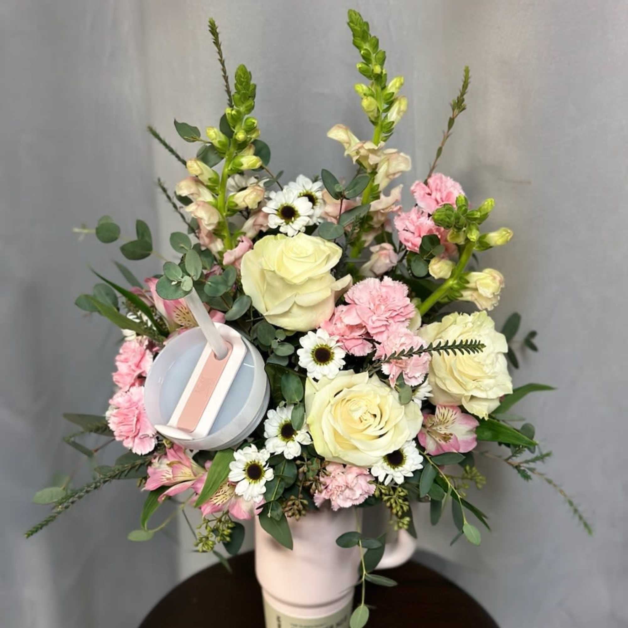 Pink and white floral arrangement in a cup-shaped container with a straw lid