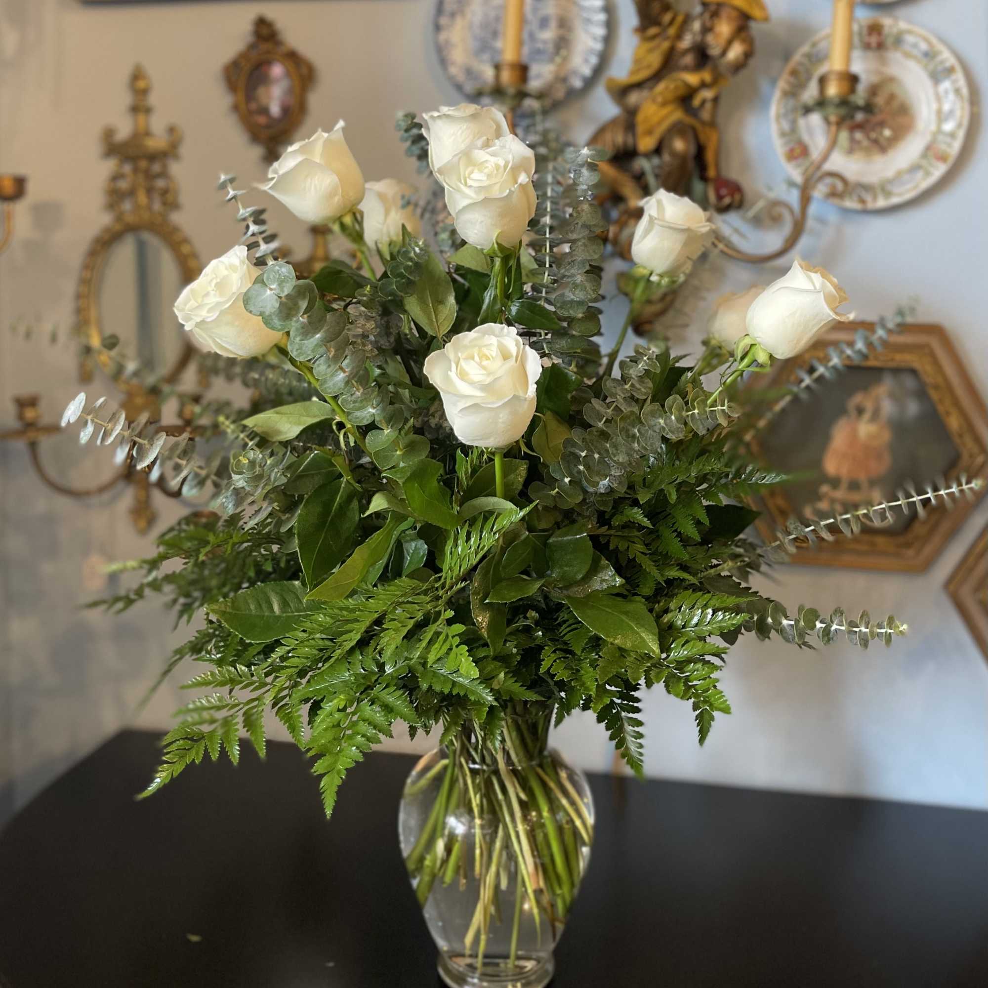 White roses arranged in a clear glass vase with greenery