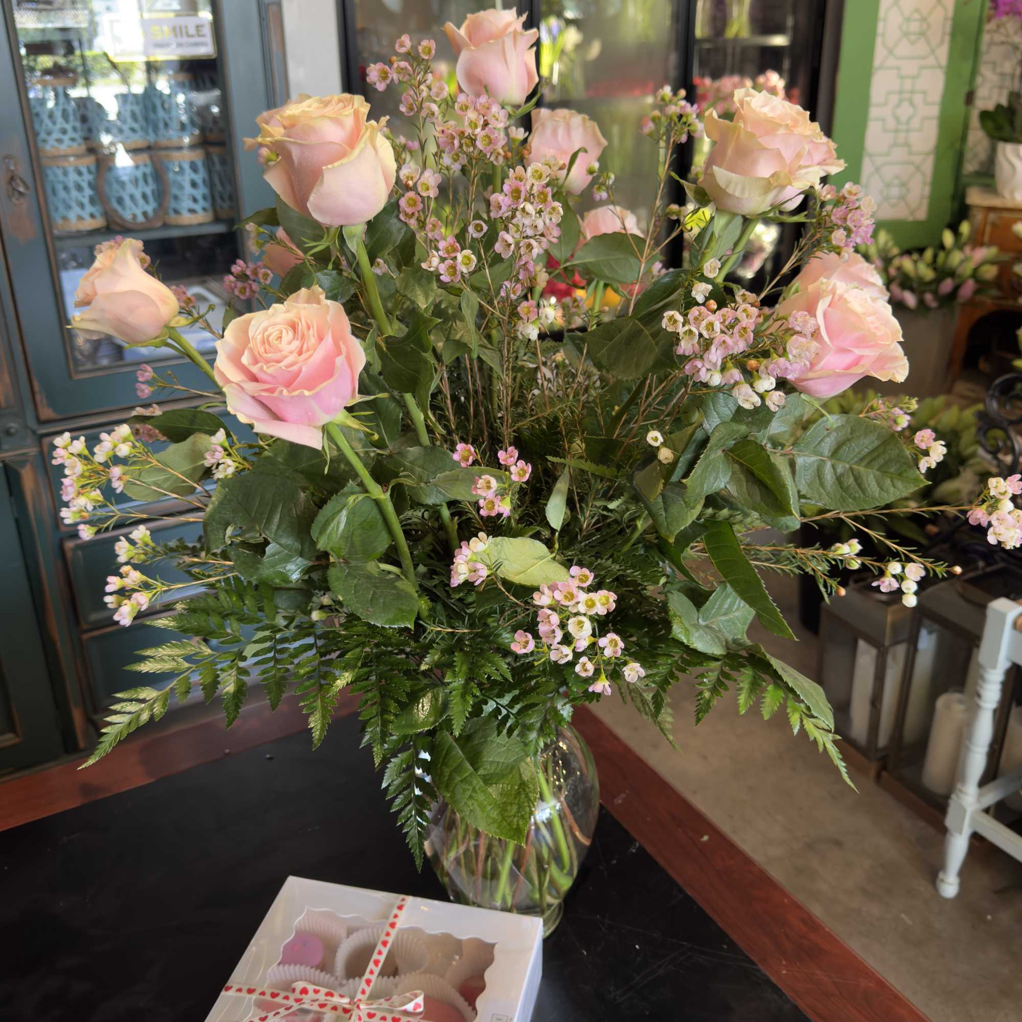Pink roses and tiny pink filler flowers in a glass vase with a box of chocolates